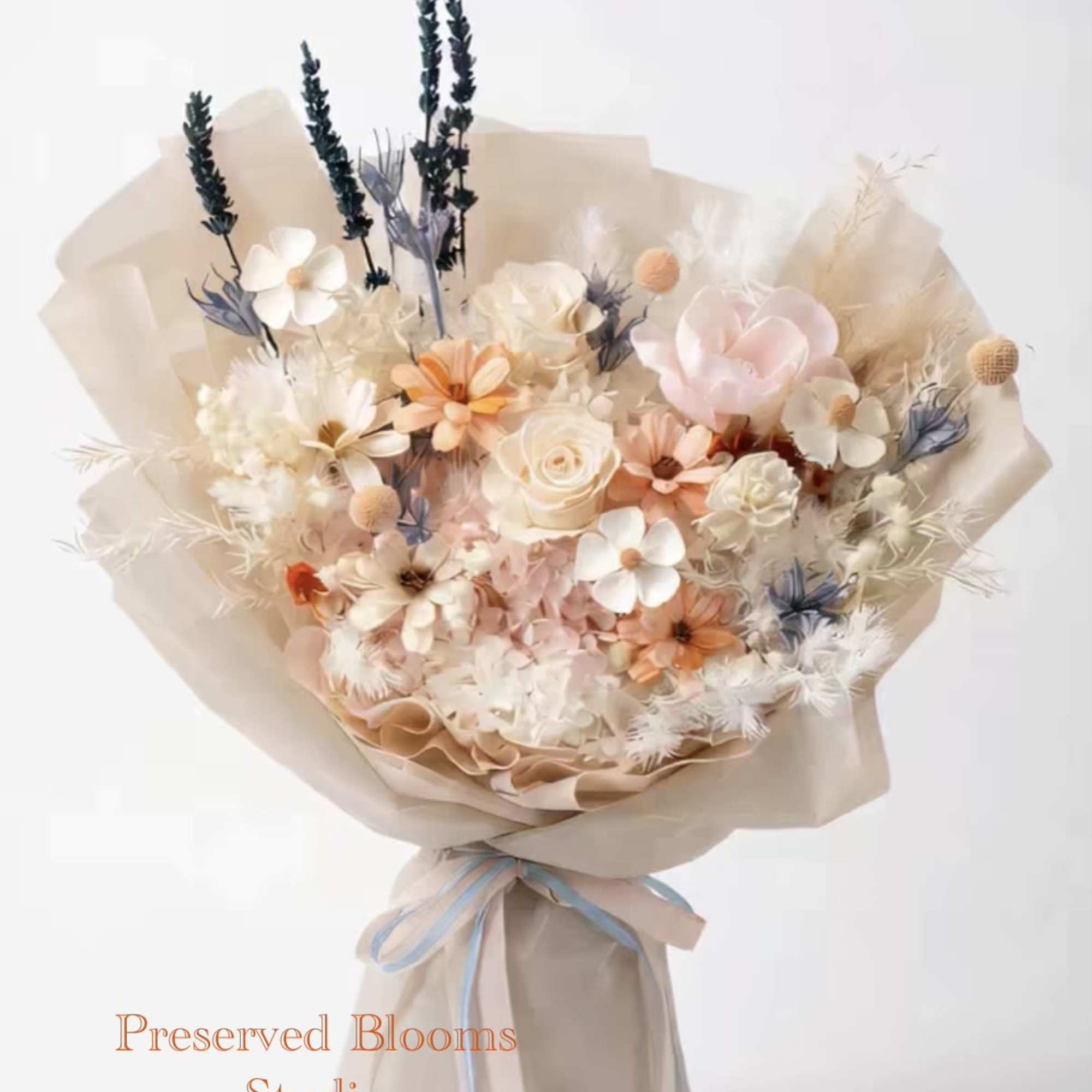 Pastel bouquet of preserved flowers wrapped in beige paper with blue and peach ribbon.