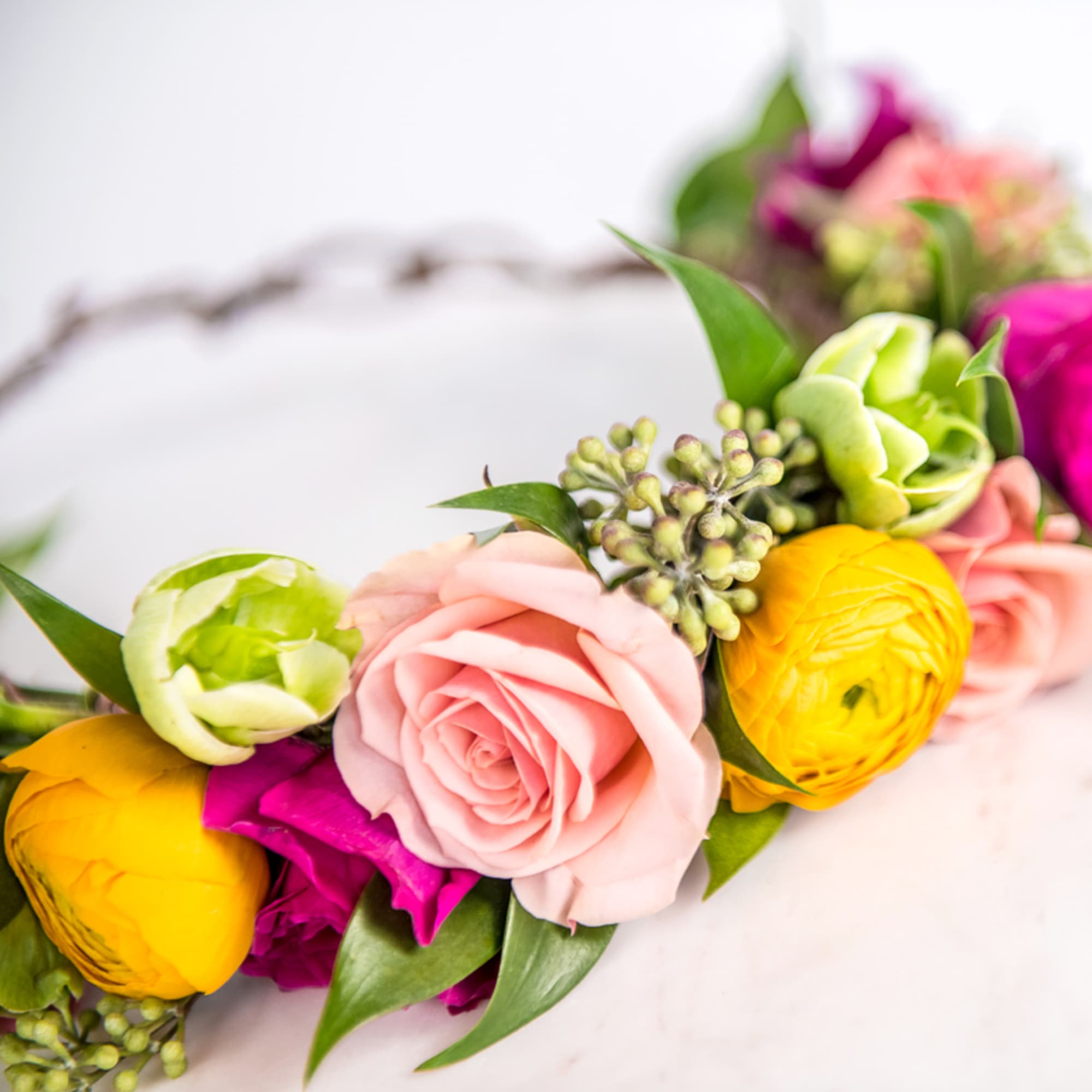 Floral crown featuring pink roses, yellow ranunculus, and green blooms on a twig base.