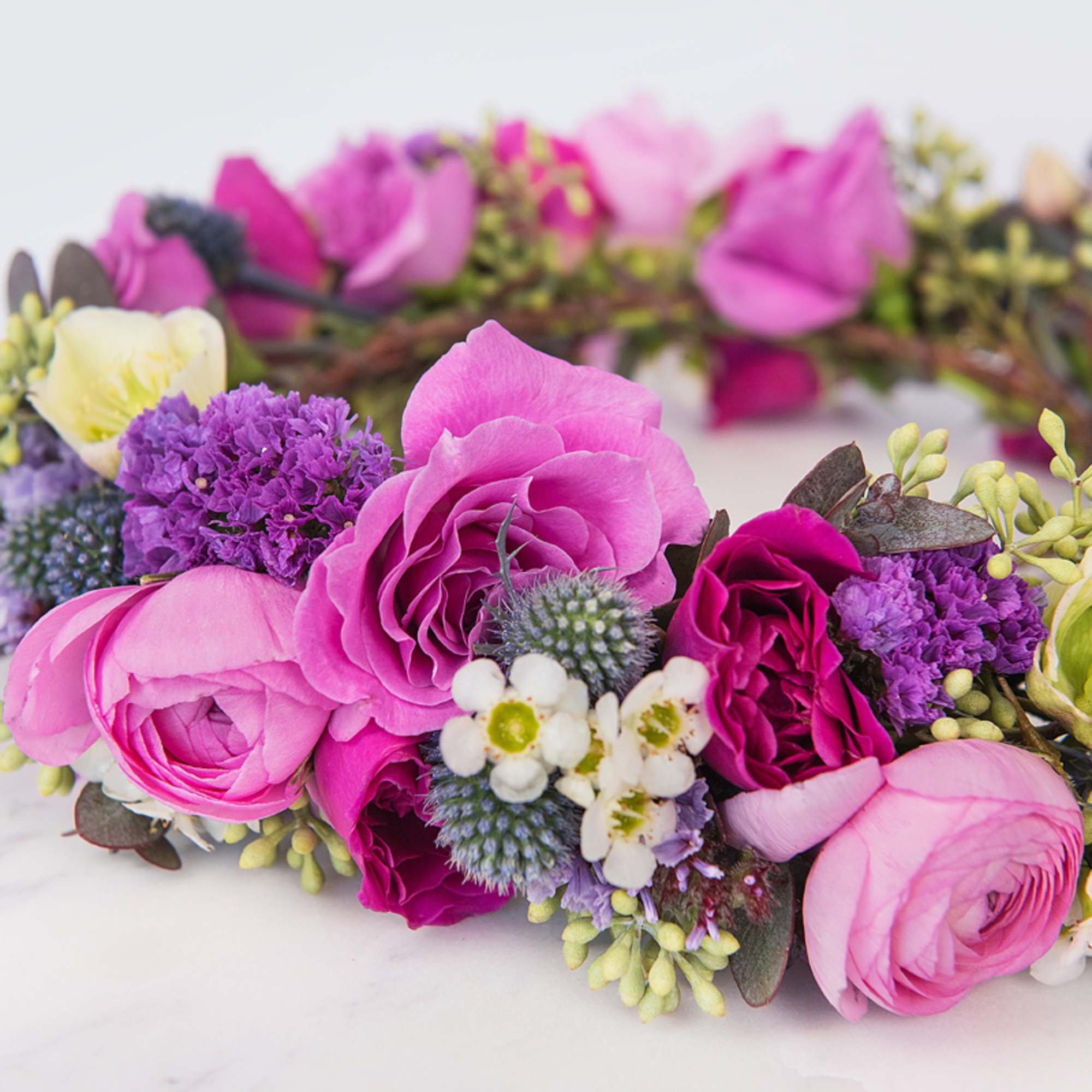 Floral crown made of pink and magenta roses, ranunculus, and purple fillers arranged in a circular wreath.