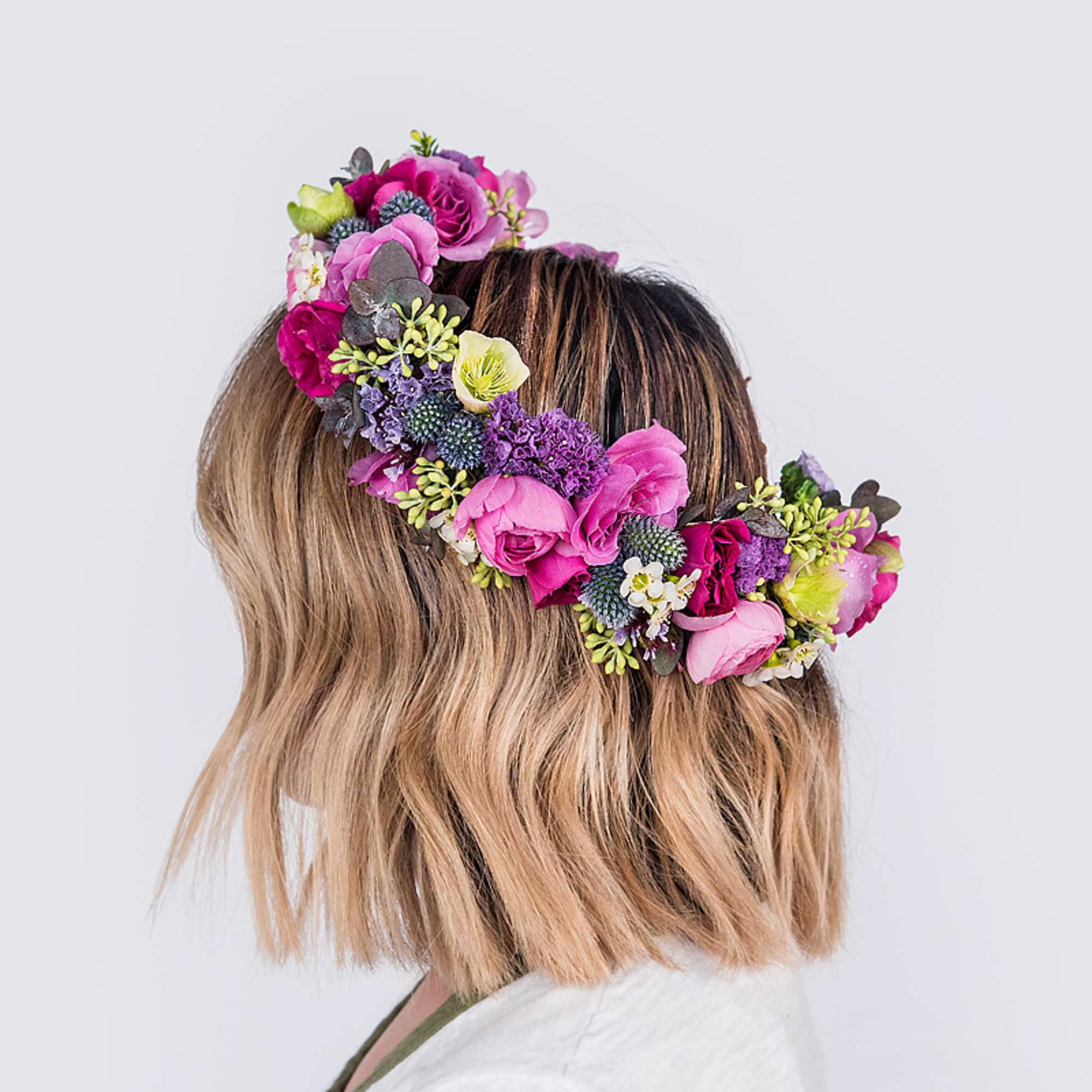 Bright flower crown of pink roses and purple blooms worn on short blonde hair.