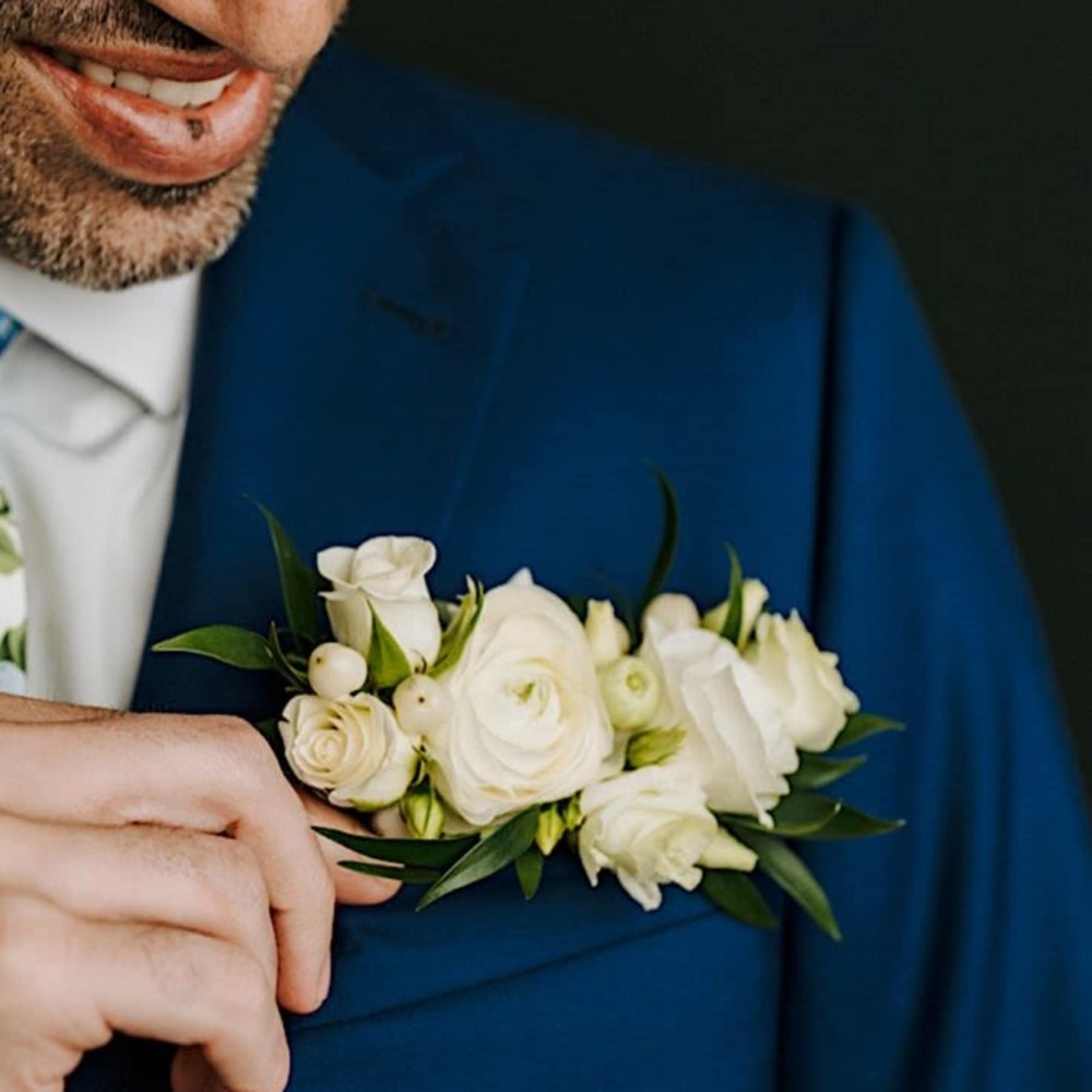 White rose boutonniere pinned to the lapel of a blue suit jacket
