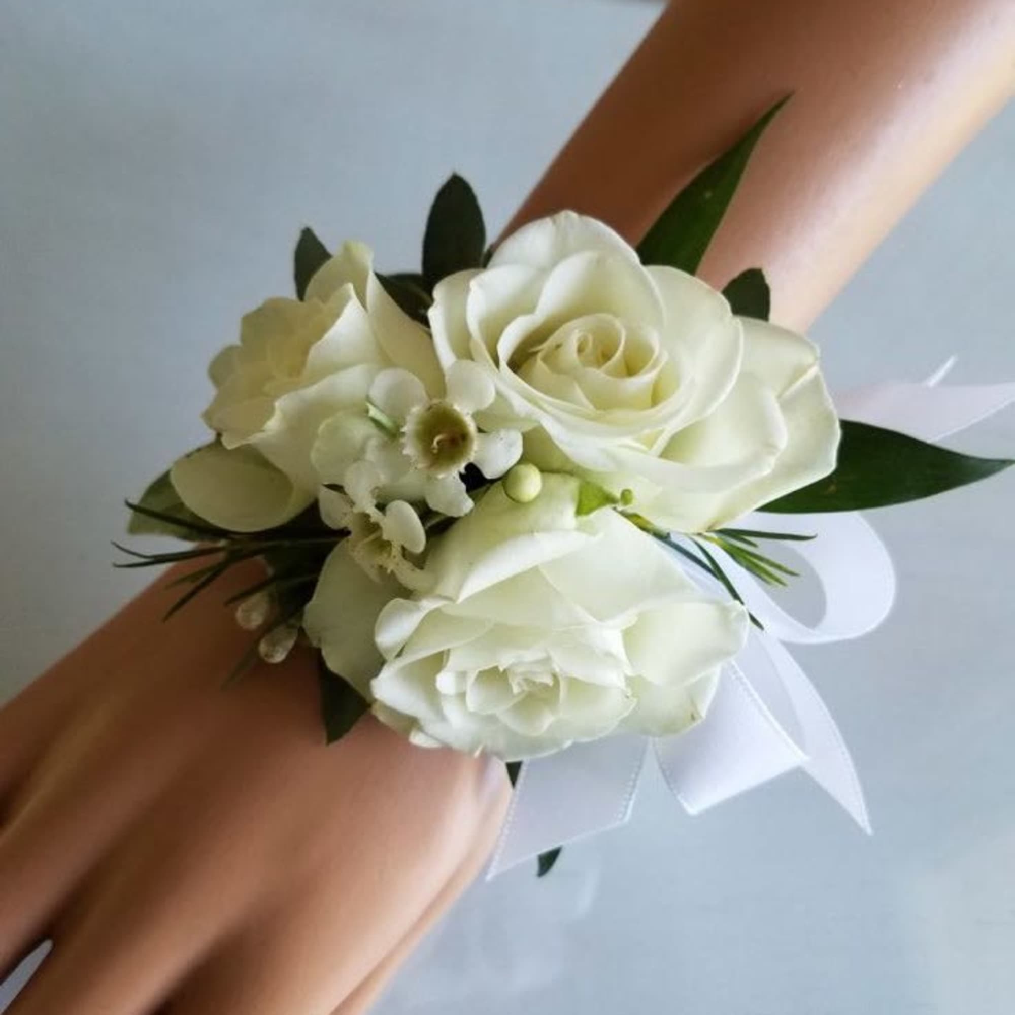 White rose wrist corsage with ribbon displayed on a mannequin hand