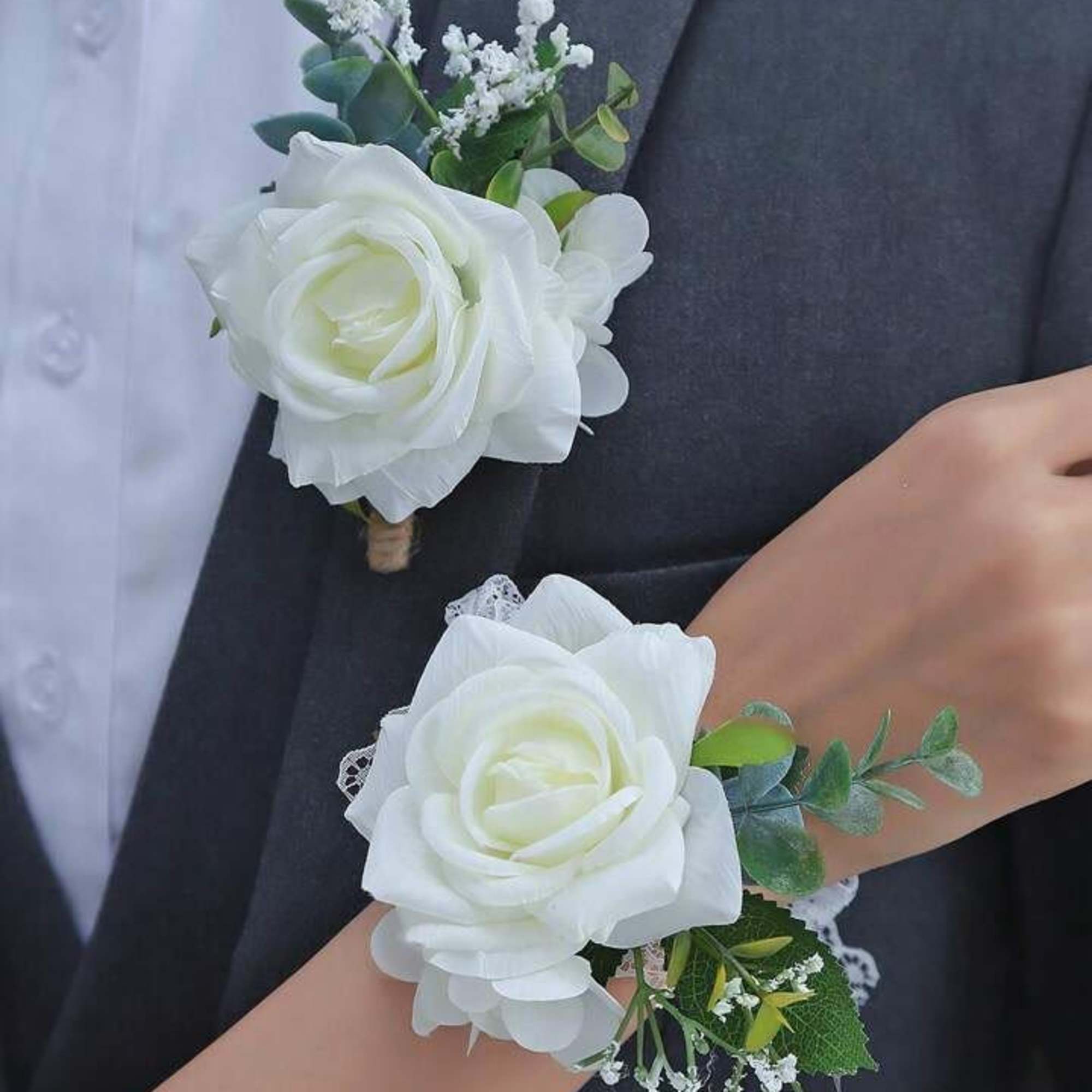 Matching white rose boutonniere and wrist corsage with small white filler flowers on formal attire.