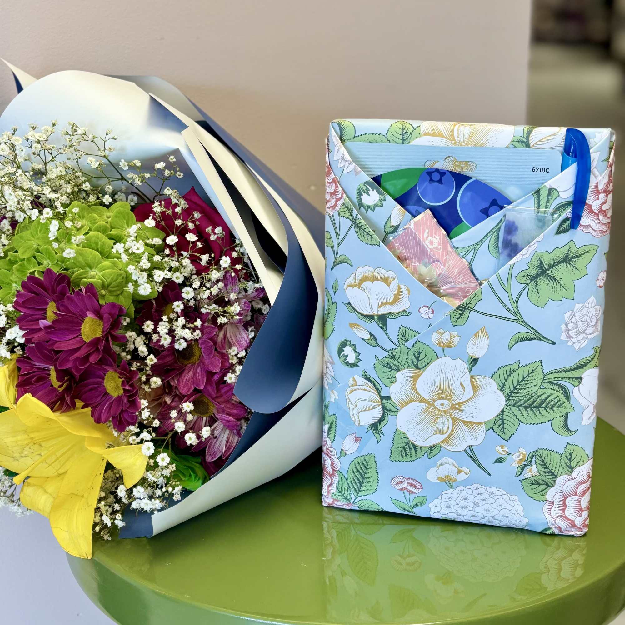 Bouquet of purple and yellow flowers beside a floral-print gift pouch on a green table