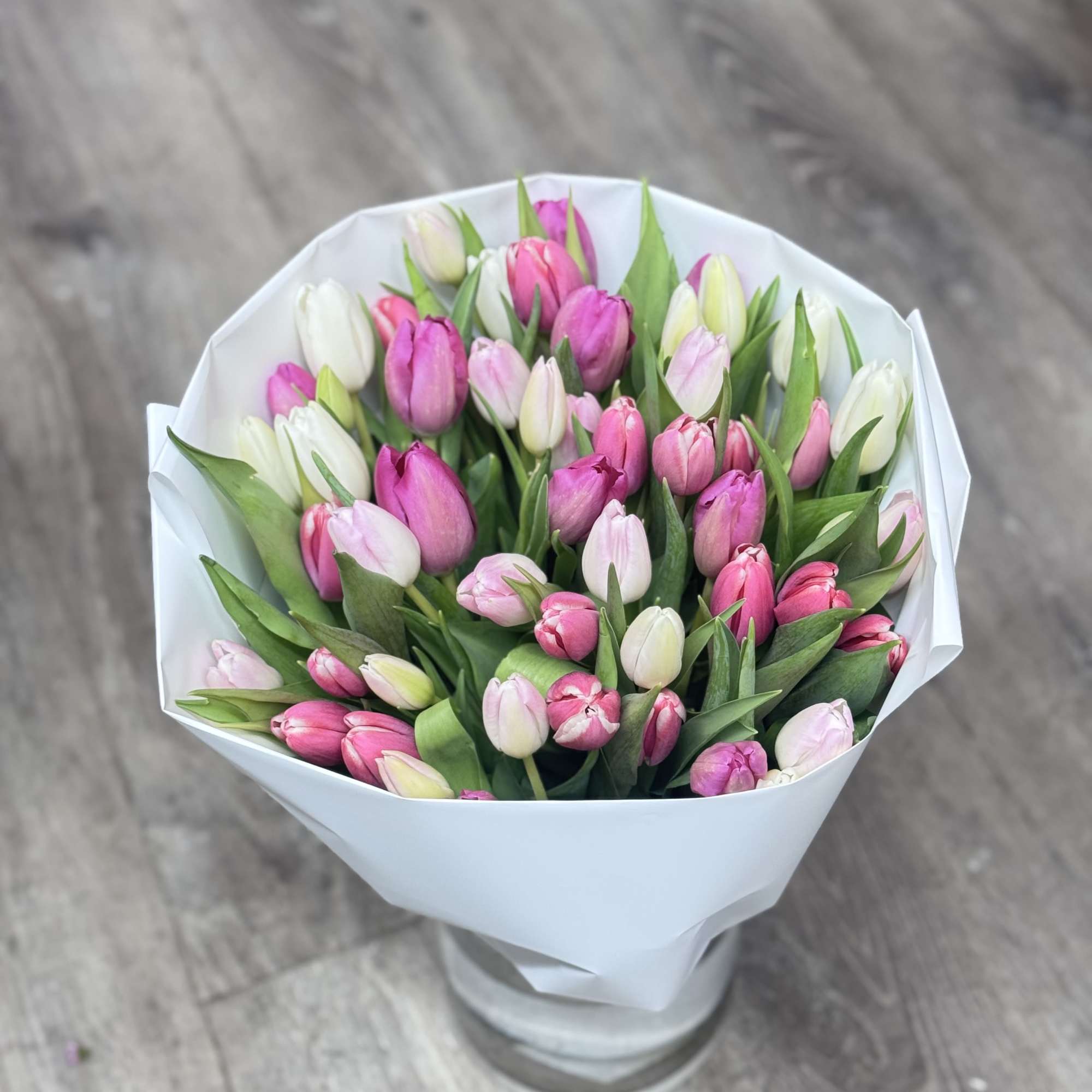 Bouquet of pink and white tulips wrapped in white paper and displayed in a clear glass vase