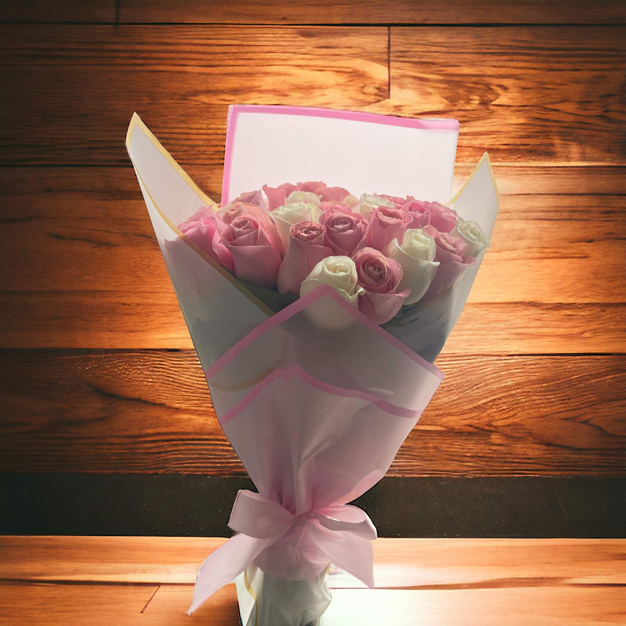 Hand-tied bouquet of pink and white roses wrapped in pastel paper with a pink ribbon bow.