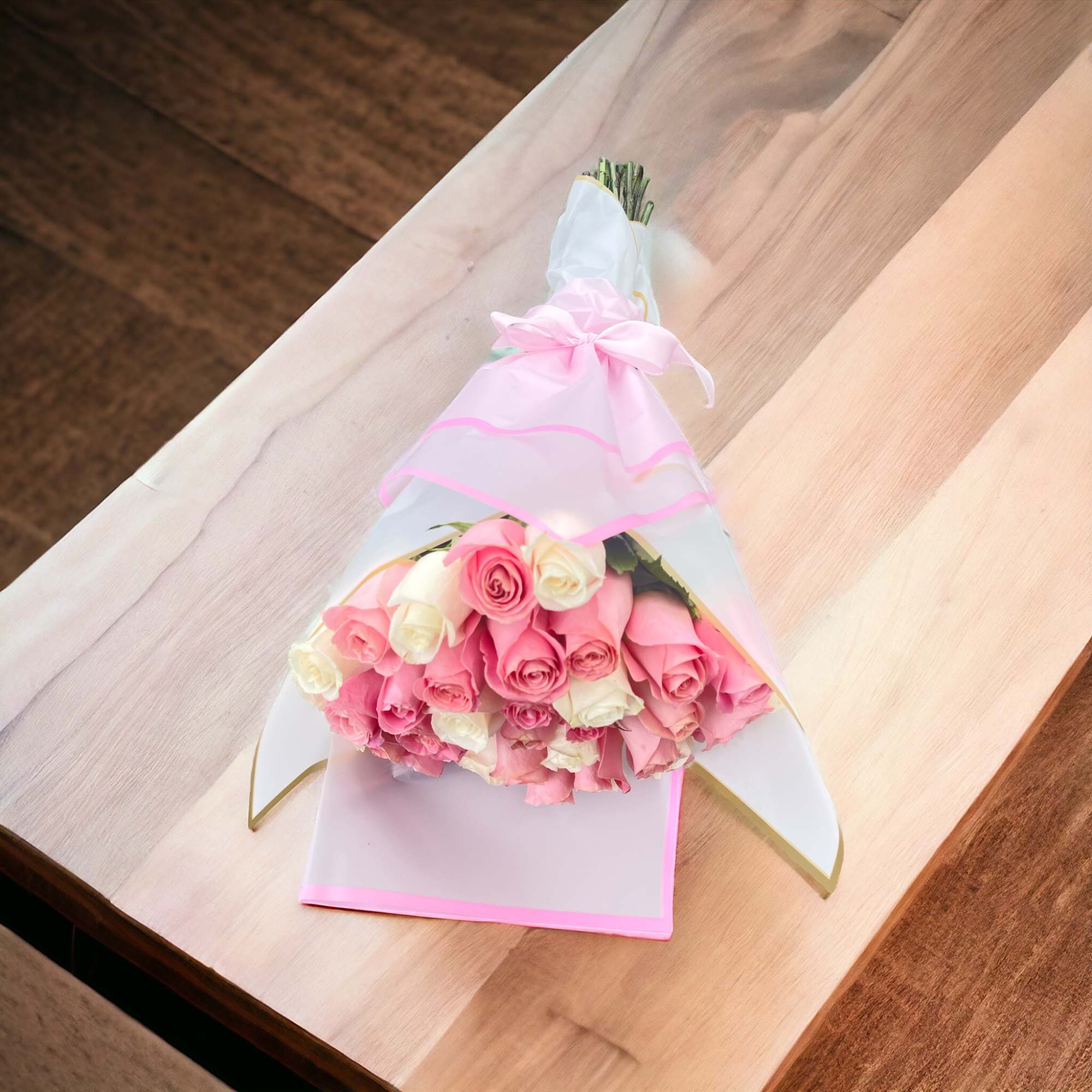 Wrapped bouquet of pink and cream roses tied with a pink ribbon on a wooden surface