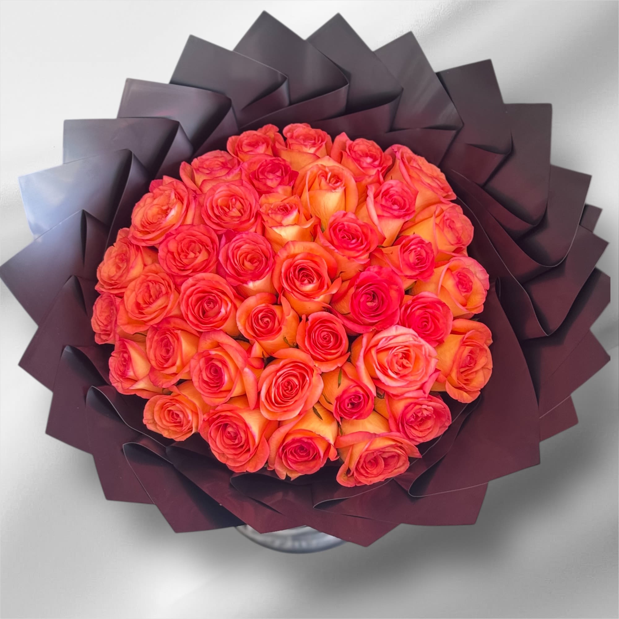 Round bouquet of orange and hot pink roses wrapped in dark, angular paper