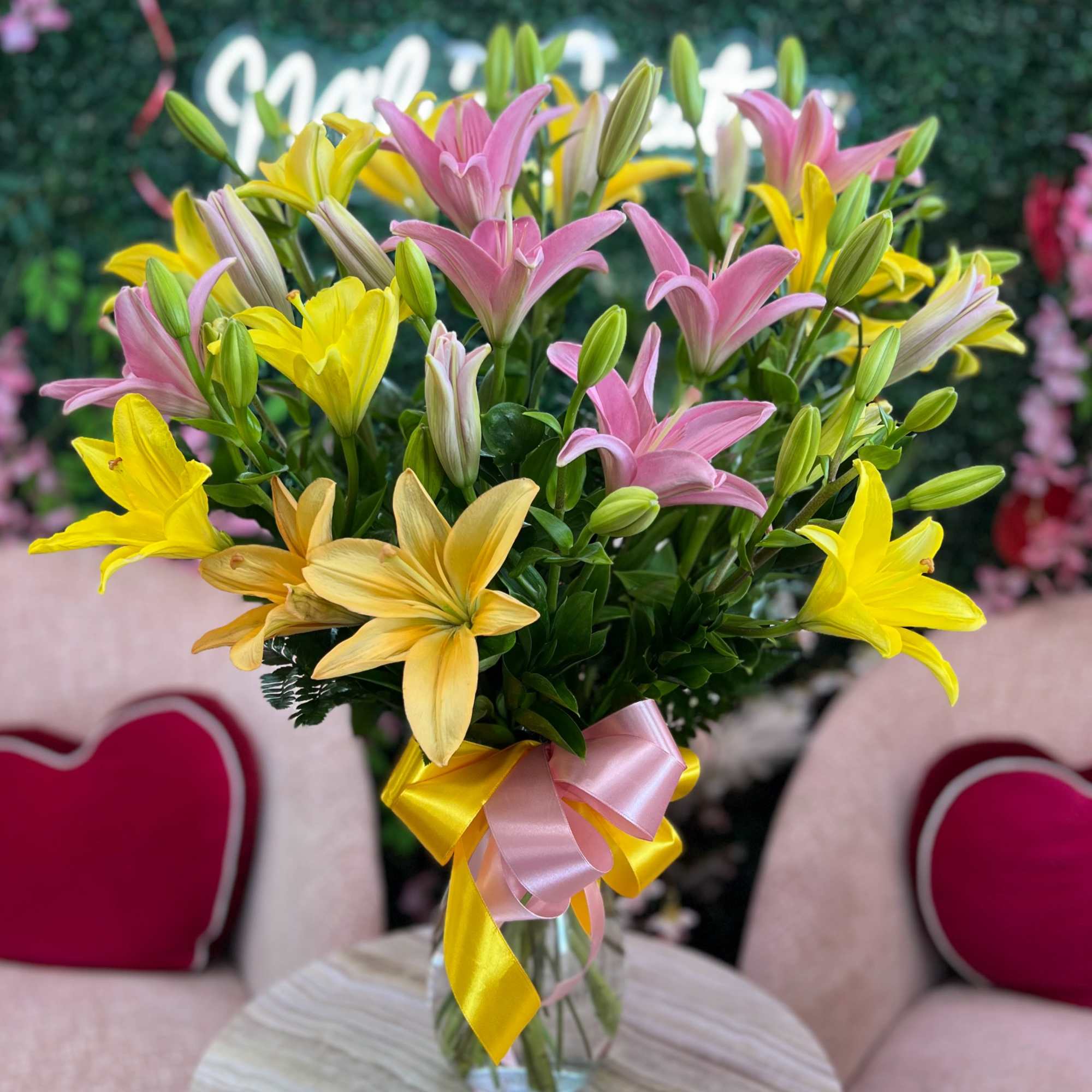 Tall arrangement of pink and yellow lilies in a clear glass vase with pink and yellow ribbon bow