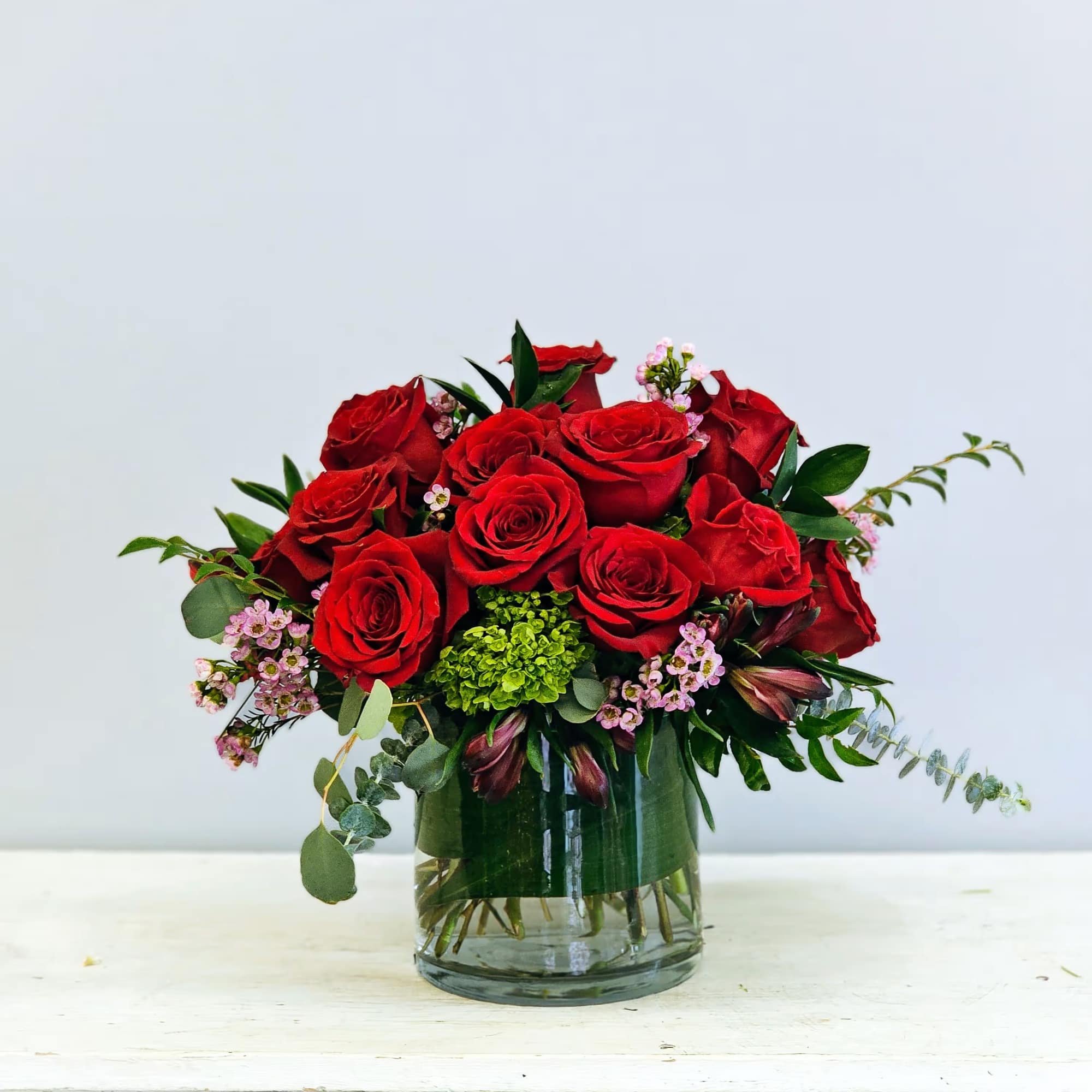 18 beautiful red roses in a short cylinder with filler and greenery.