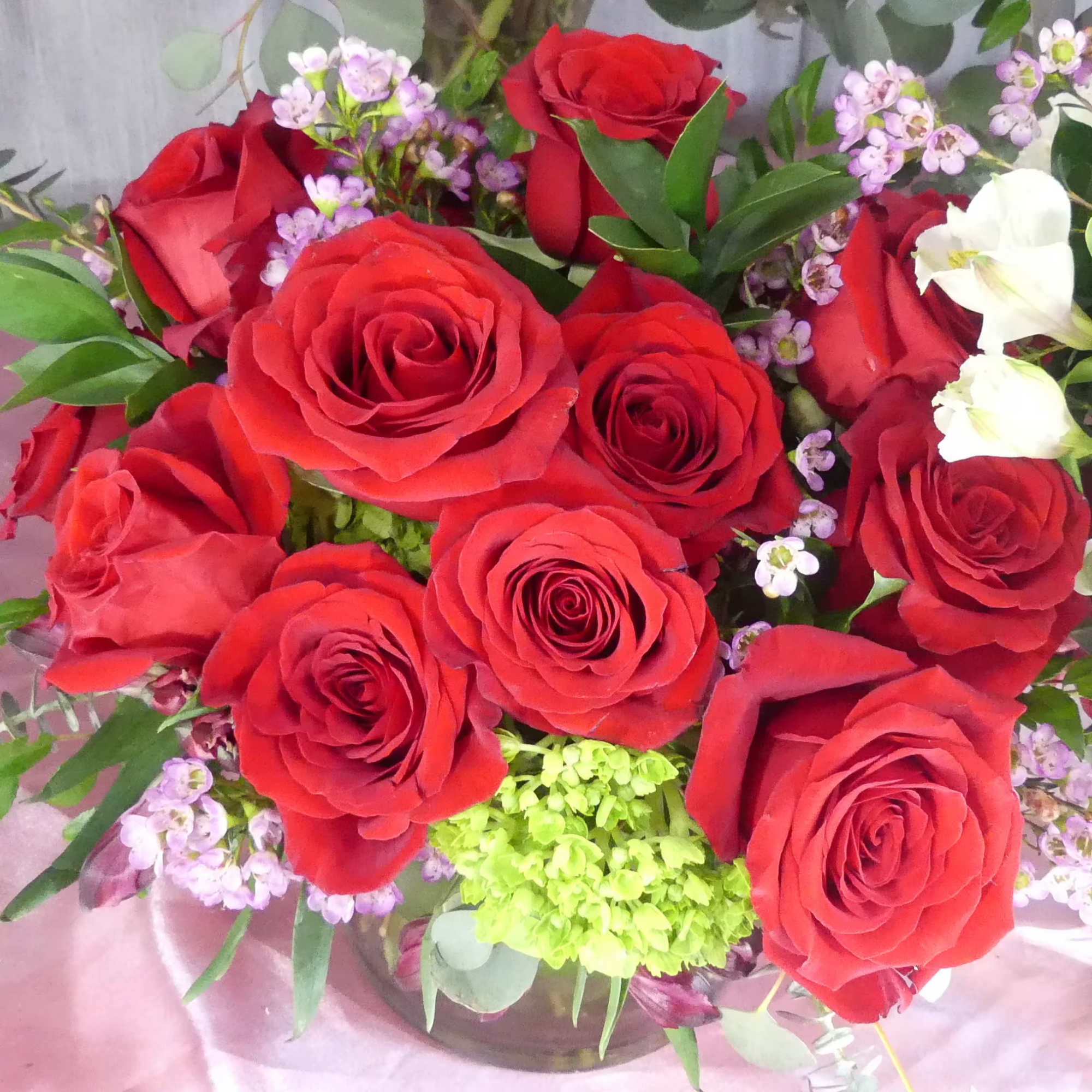 18 beautiful red roses in a short cylinder with filler and greenery.