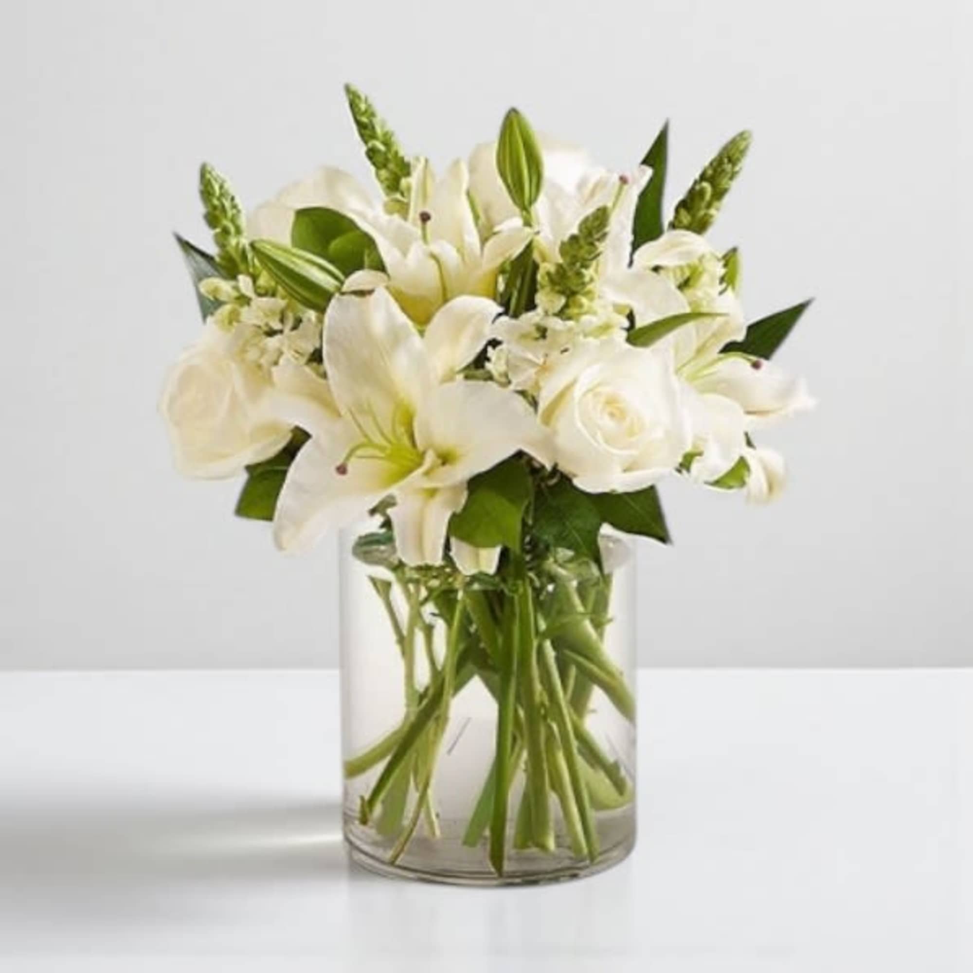 White lilies and roses arranged in a clear glass vase