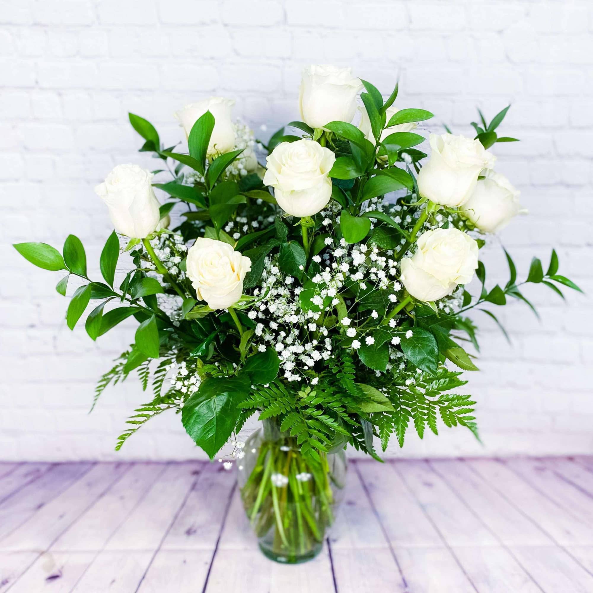 White roses arranged in a clear glass vase with baby's breath and greenery