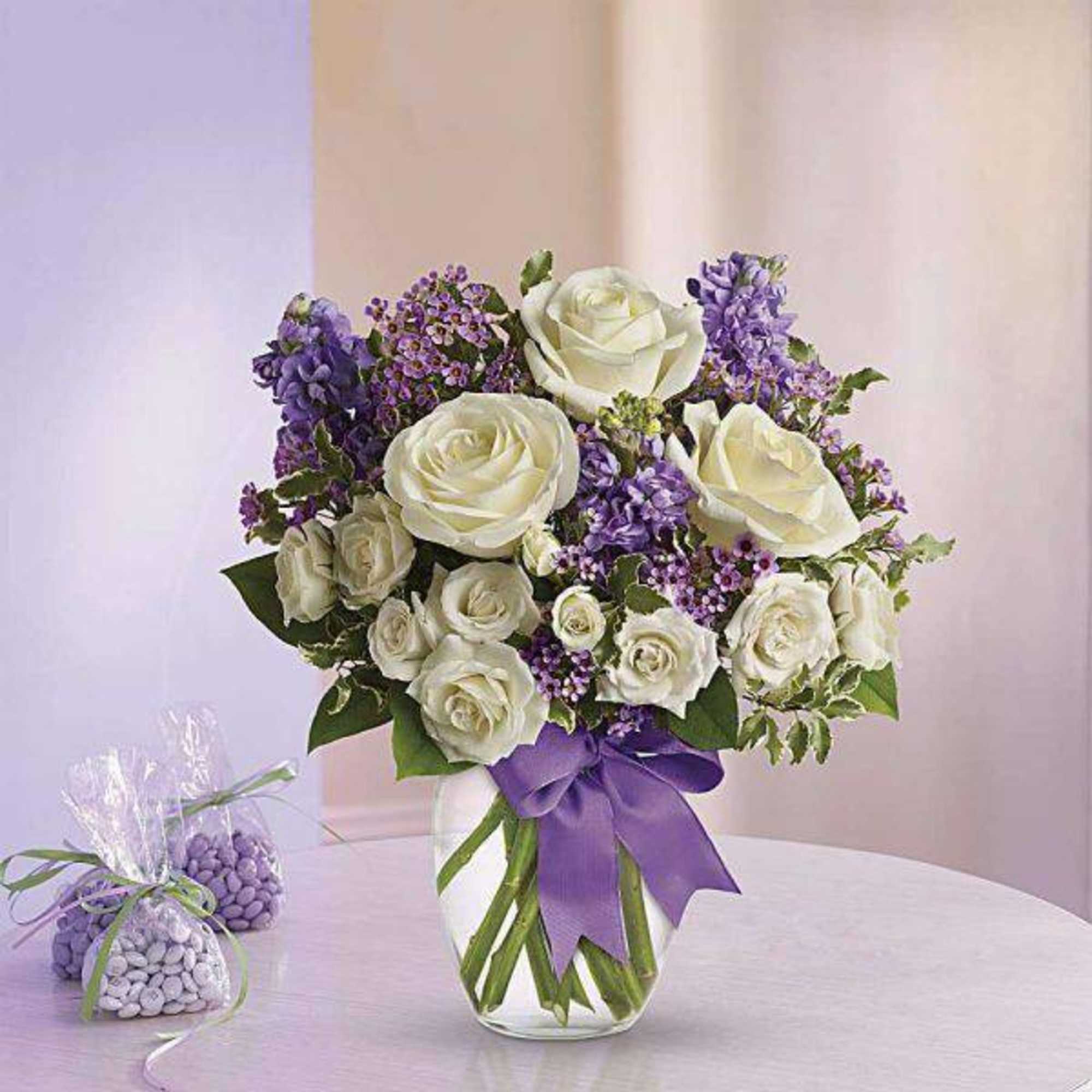 White roses and purple flowers in a glass vase with a purple ribbon