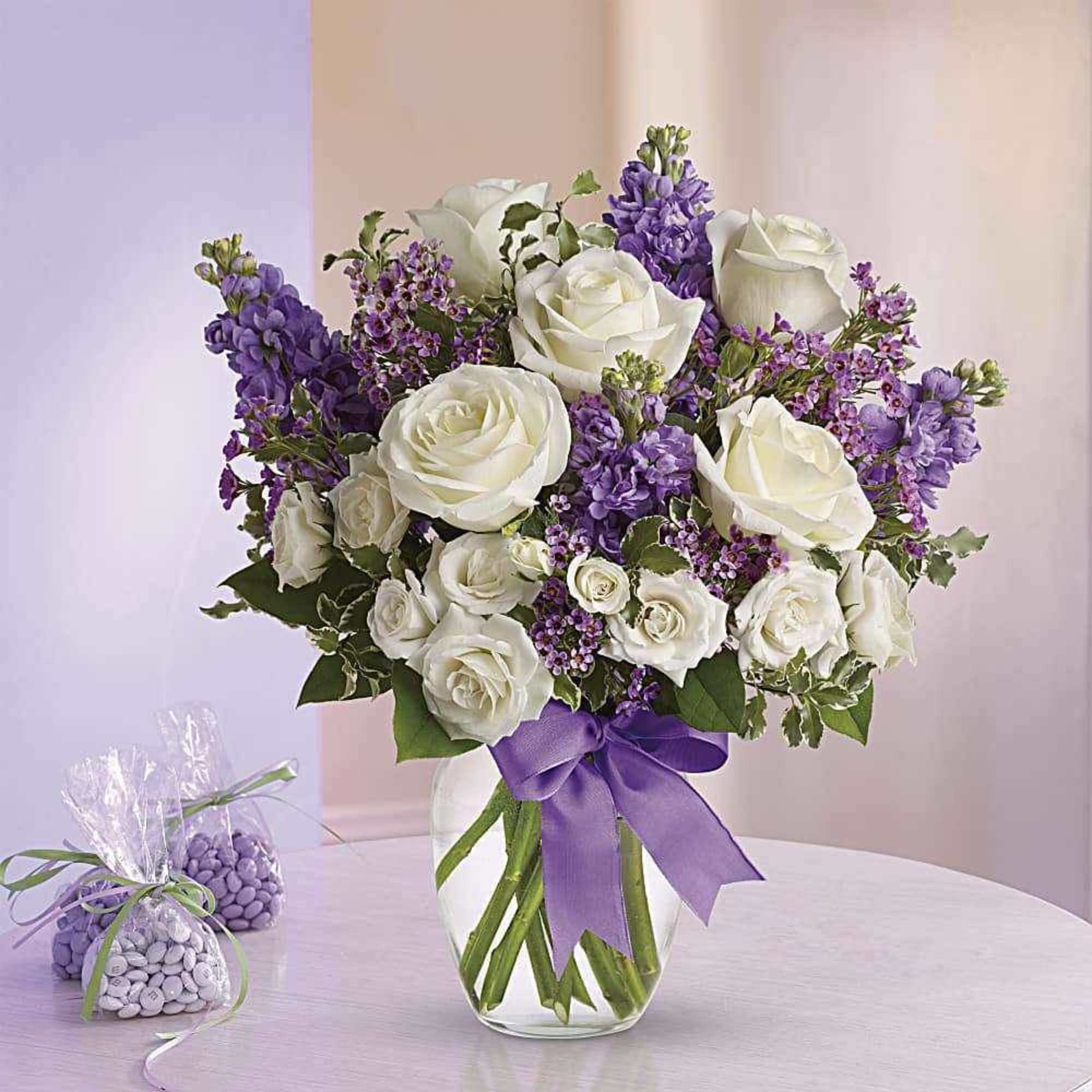 White roses and purple flowers in a glass vase with a purple ribbon