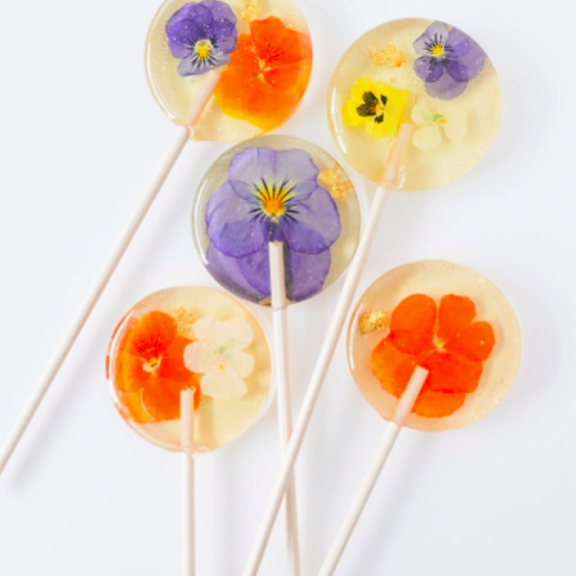Set of five clear round lollipops with colorful pressed flowers inside on white sticks
