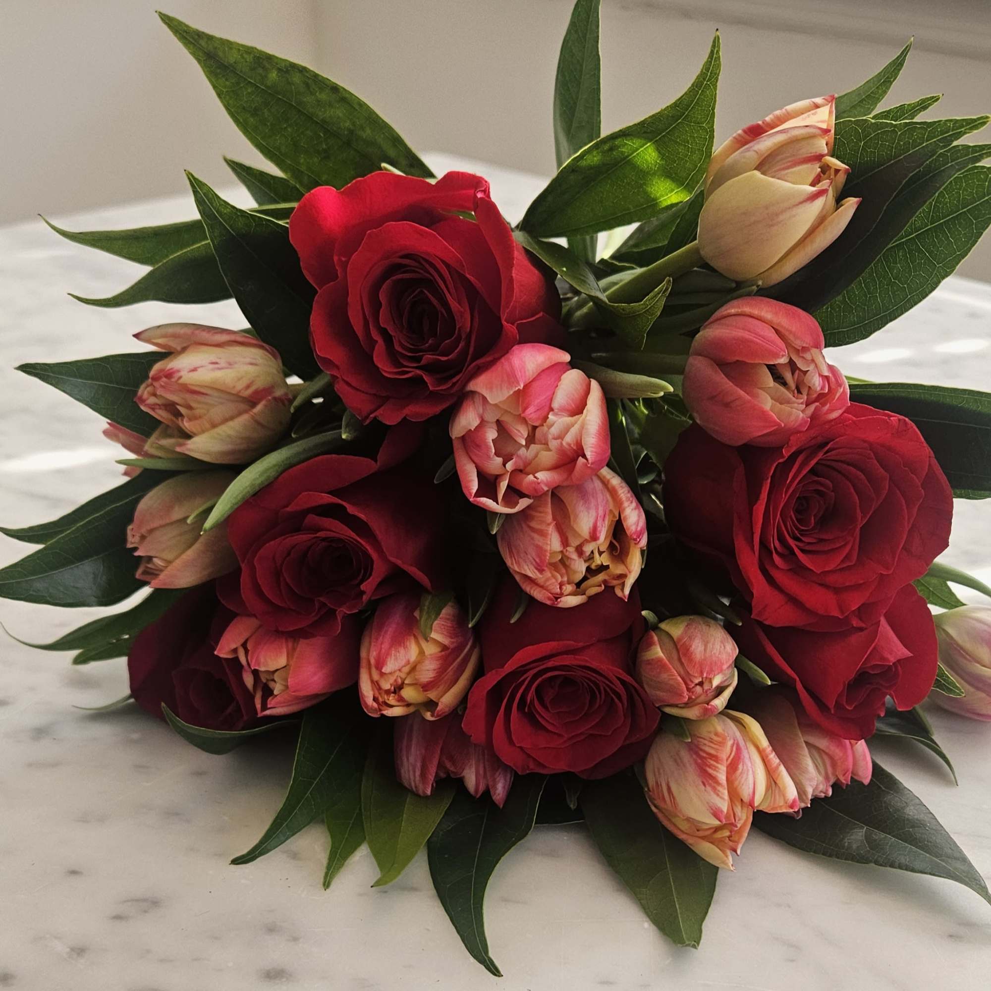 Hand-tied bouquet of red roses and pink bi-color tulips resting on a marble surface
