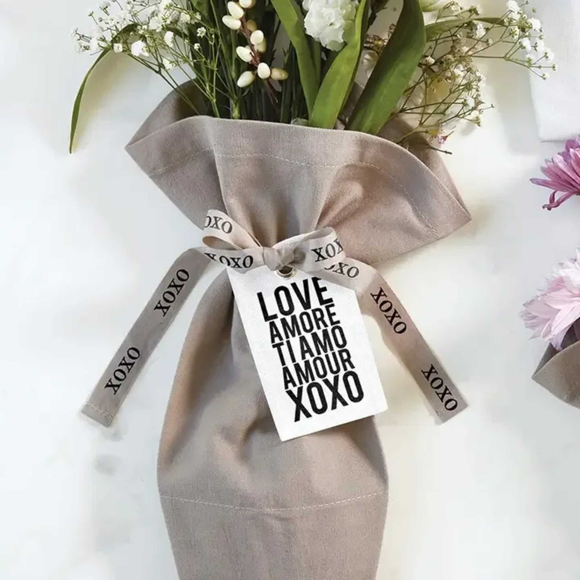 Neutral-wrapped bouquet of small white flowers with a love-themed tag and XOXO ribbon