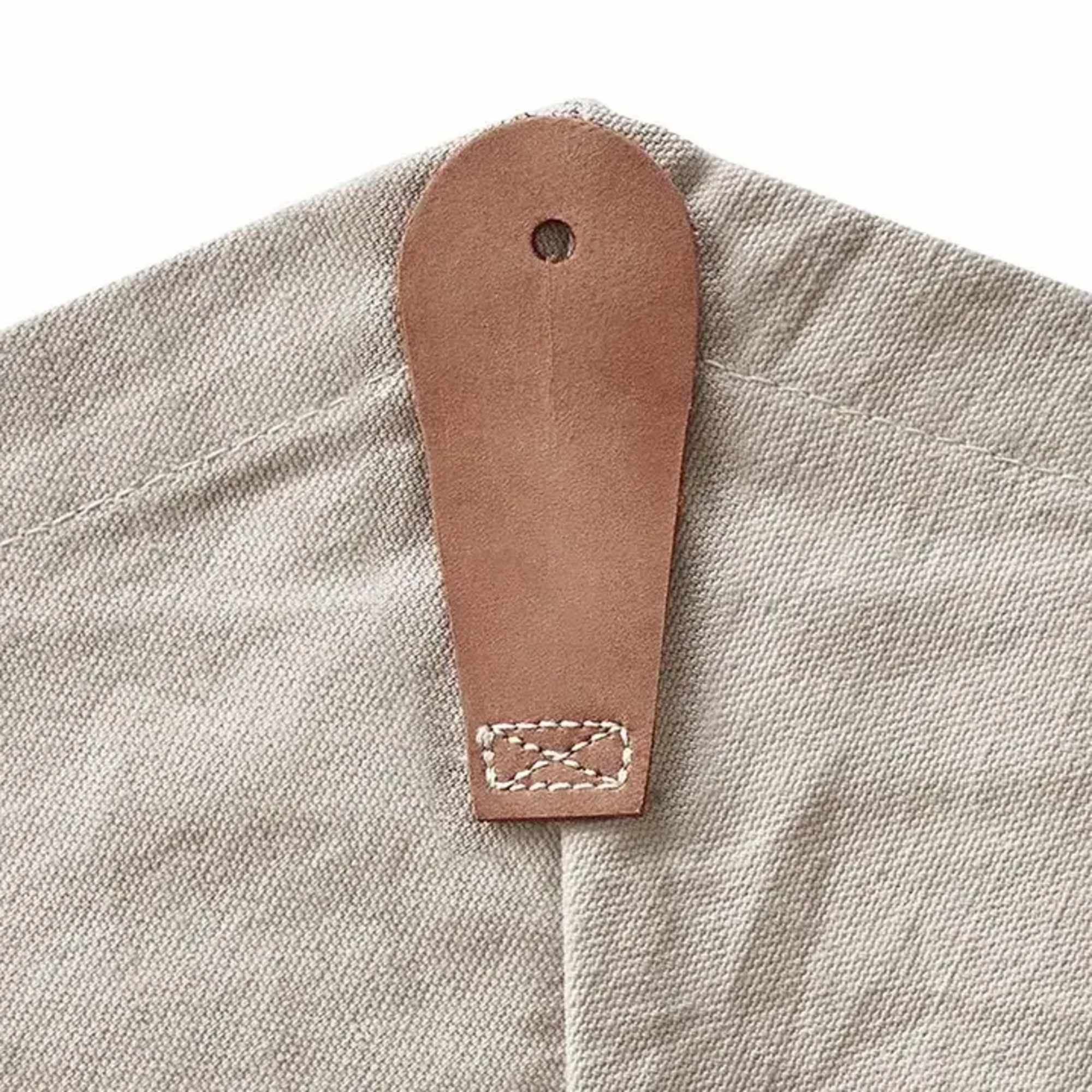 Close-up of a beige canvas fabric corner with a tan leather hanging tab and stitching