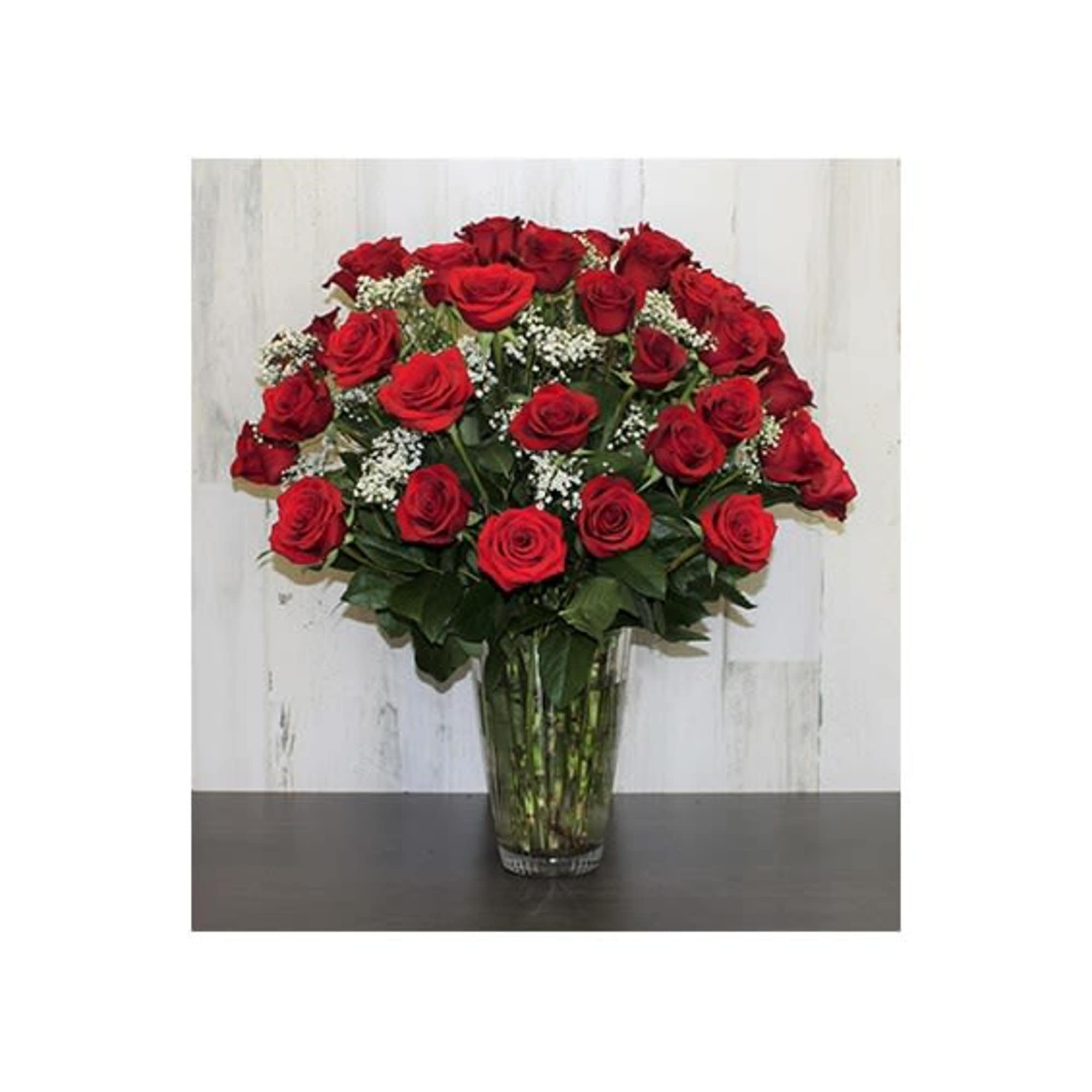 Tall arrangement of many red roses with white filler flowers in a clear glass vase