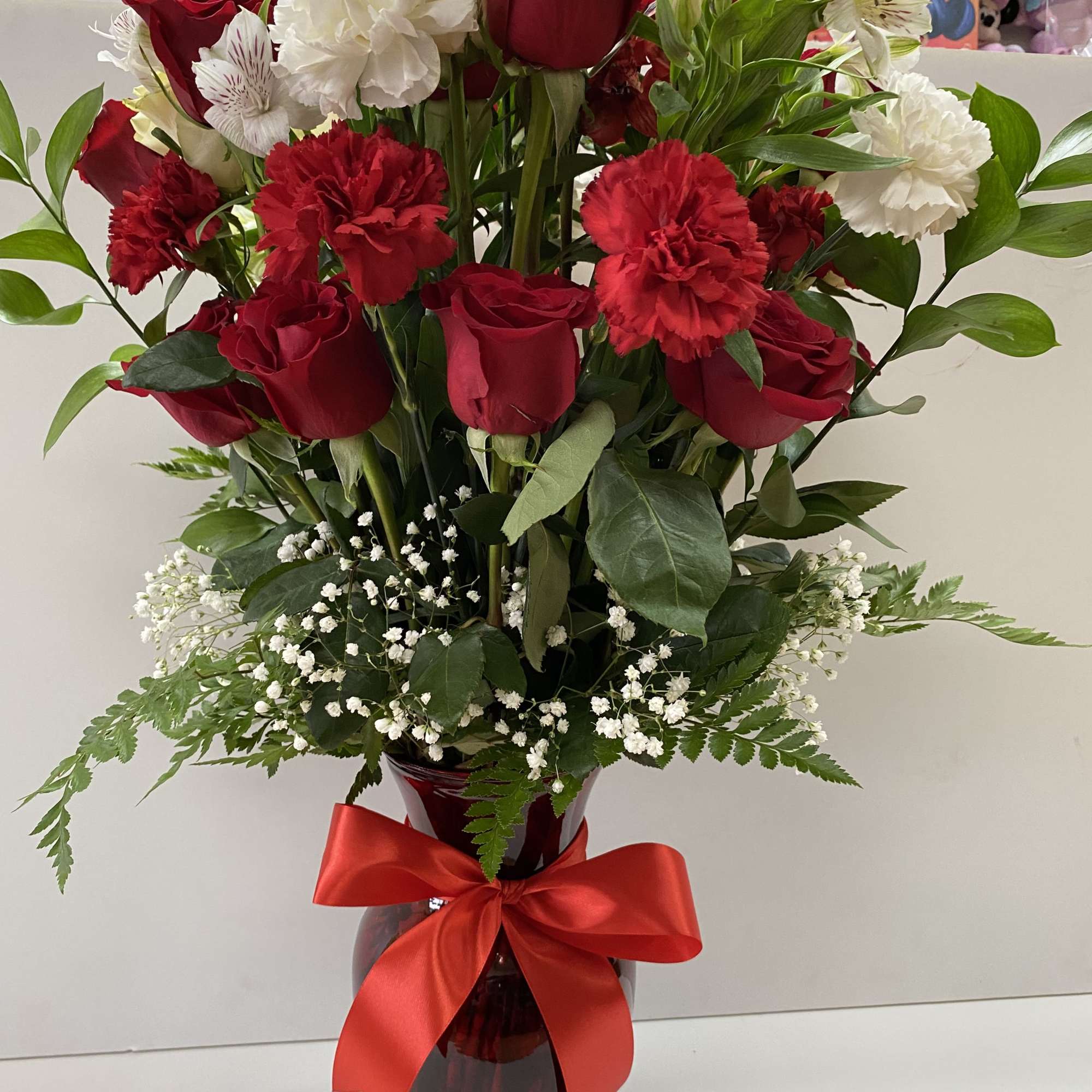 Tall arrangement of red roses and carnations with white blooms in a red vase with a red bow