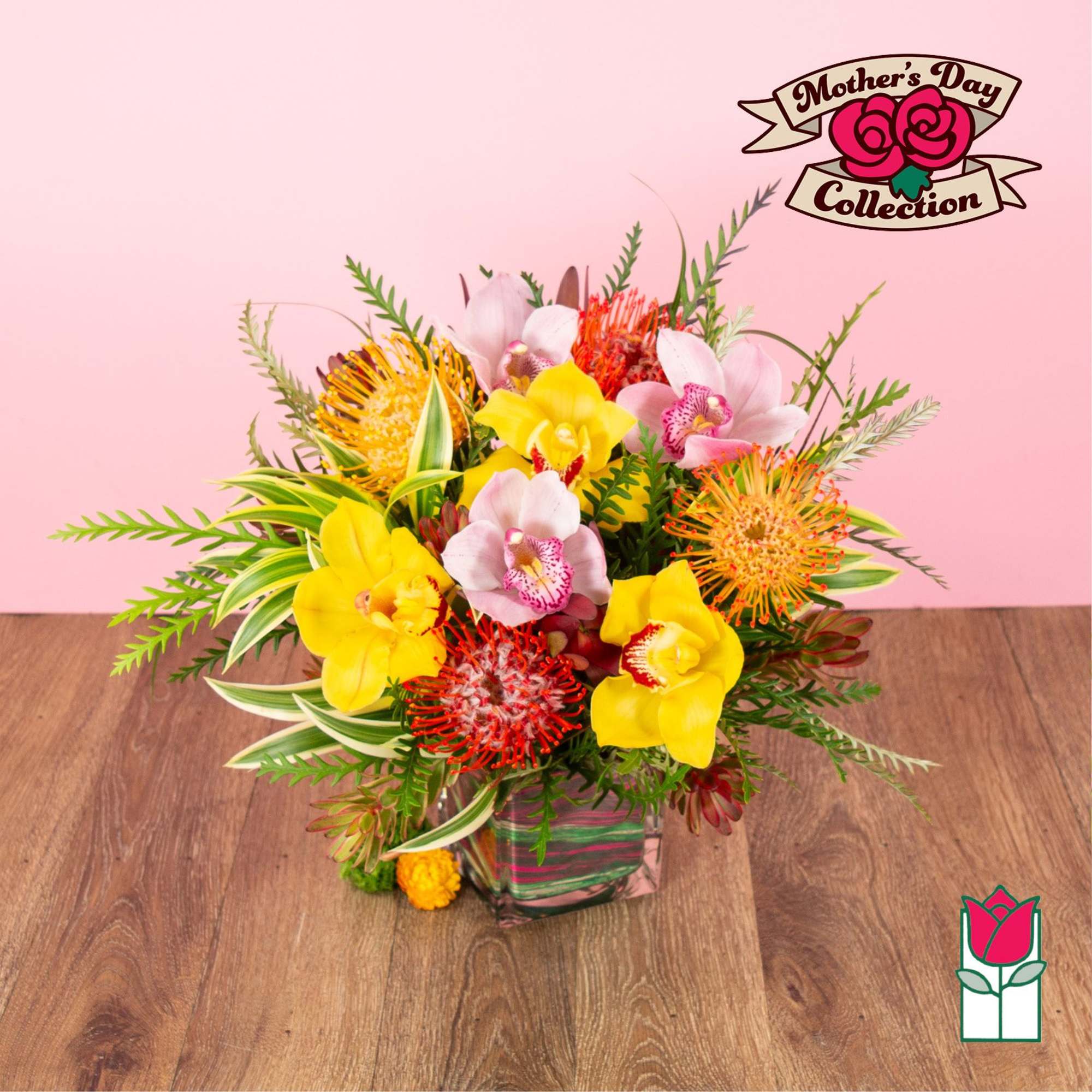 Bright arrangement of yellow and pink orchids with orange pincushion blooms in a glass cube vase.