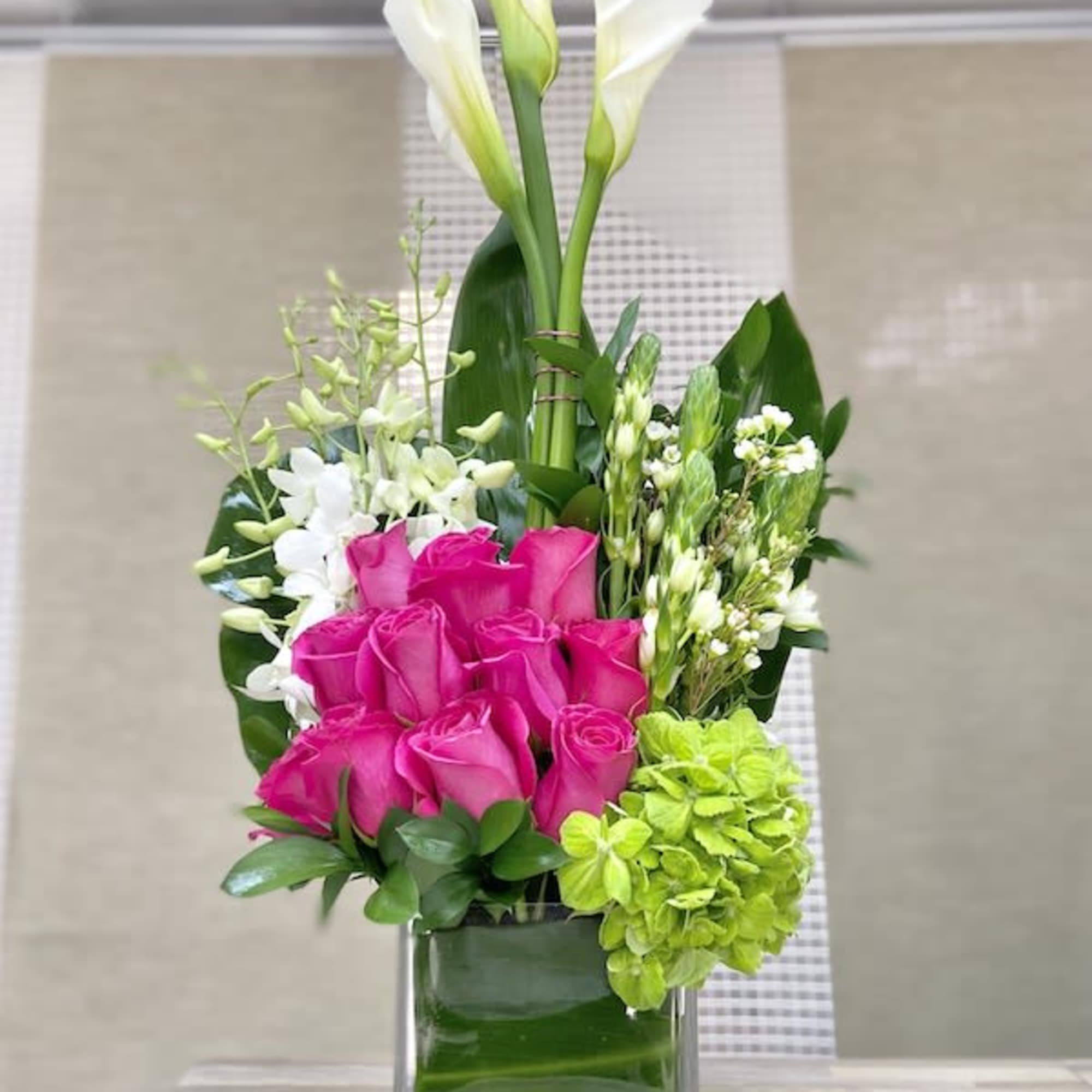 Tall modern arrangement with white calla lilies, hot pink roses, and green hydrangea in a glass cube vase