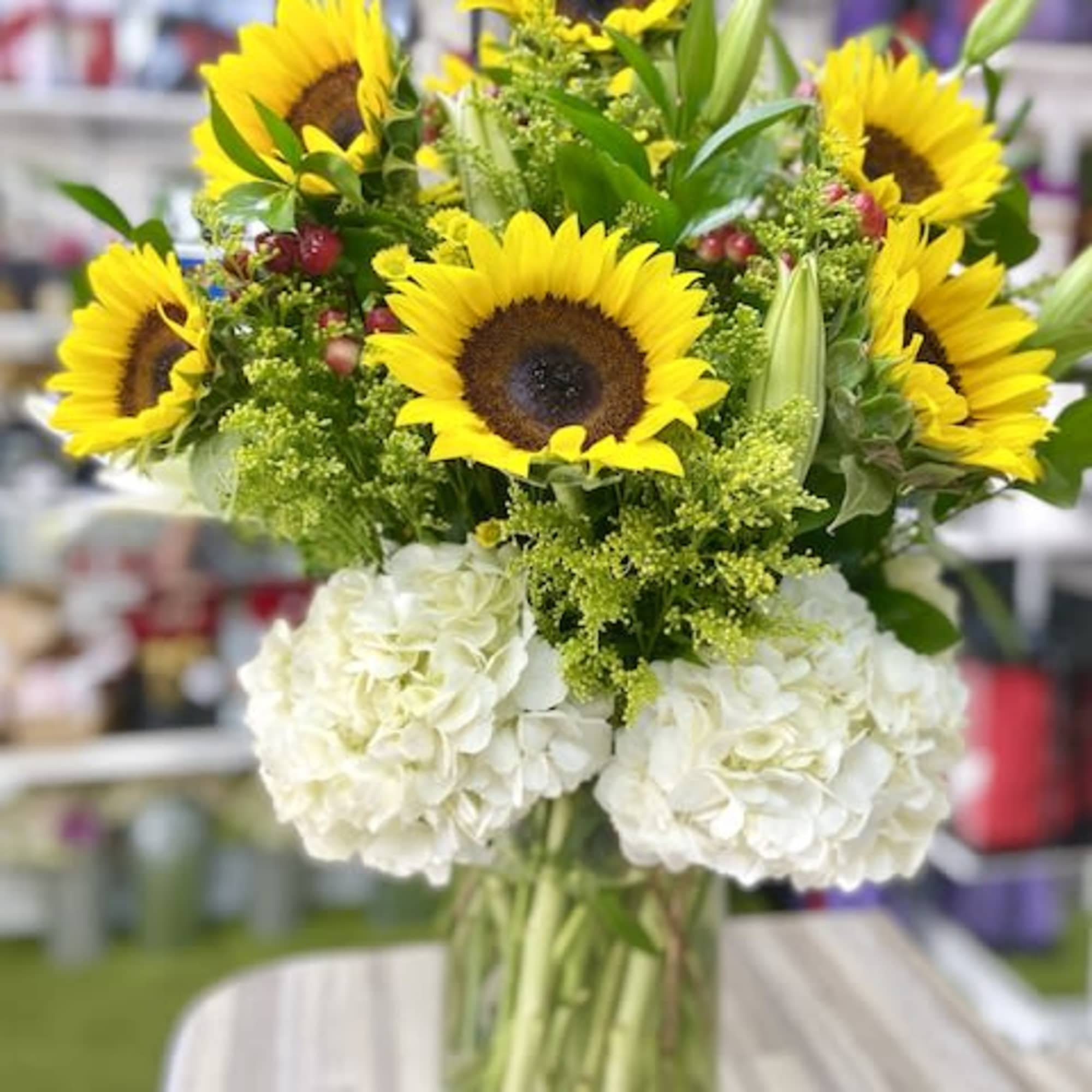 Tall arrangement of yellow sunflowers and white hydrangeas in a clear glass vase