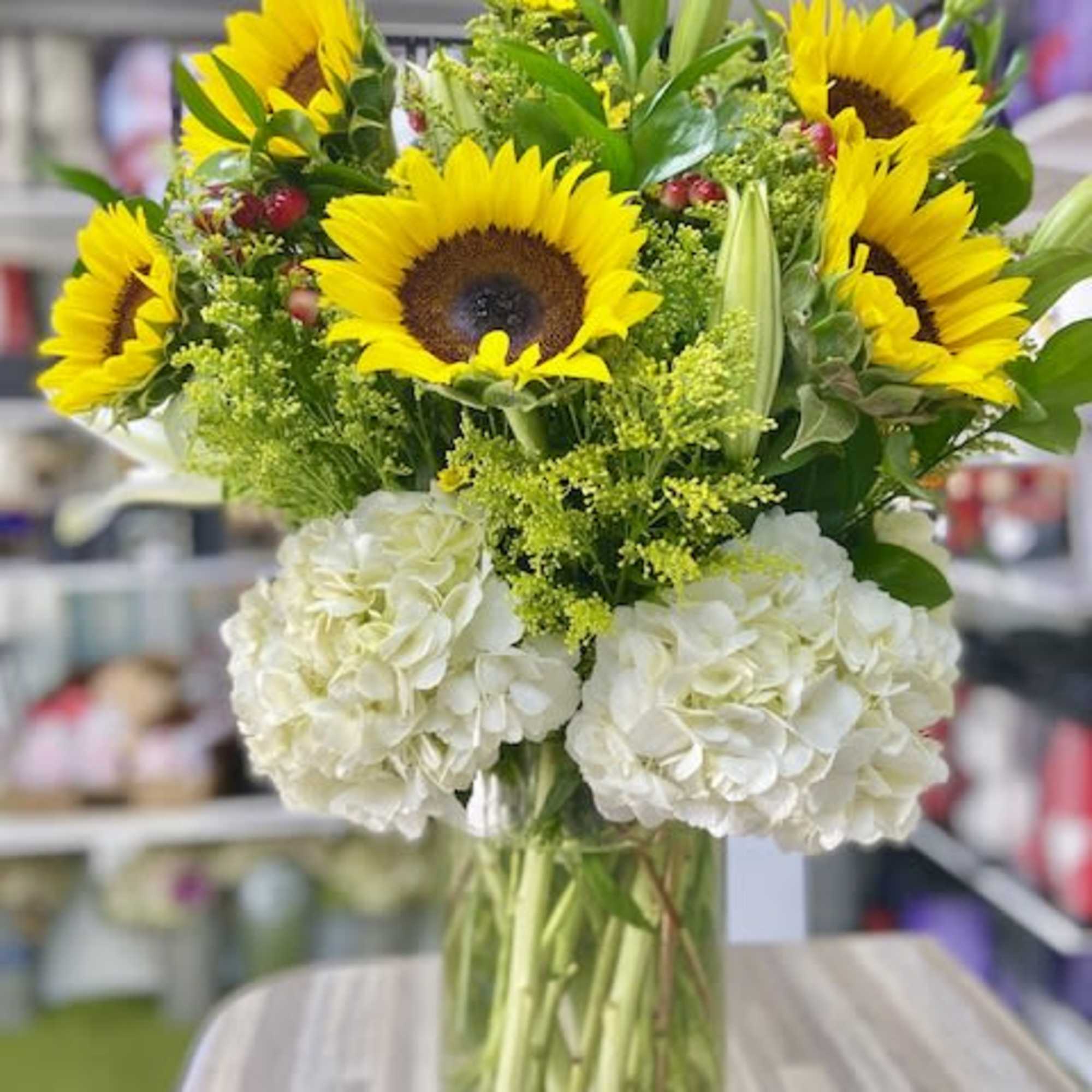 Tall bouquet of yellow sunflowers and white hydrangeas in a clear glass vase