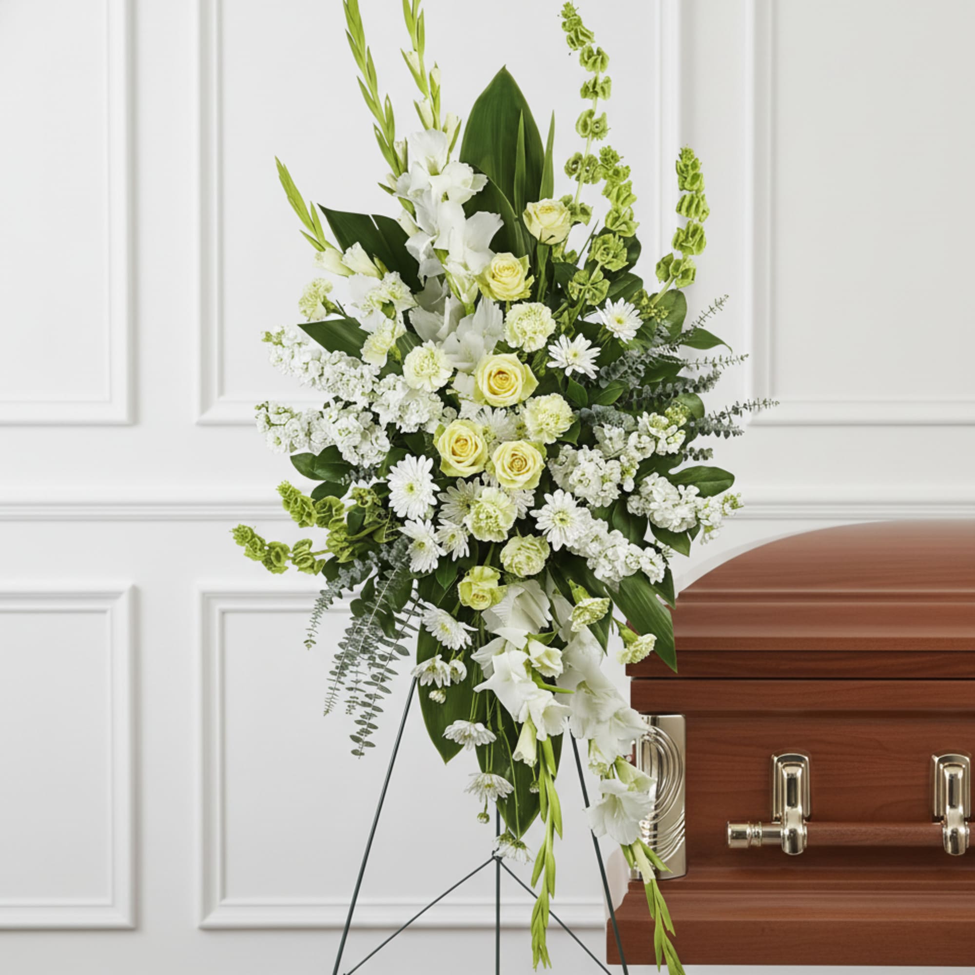 Tall white and pale yellow standing floral spray on an easel beside a wood casket