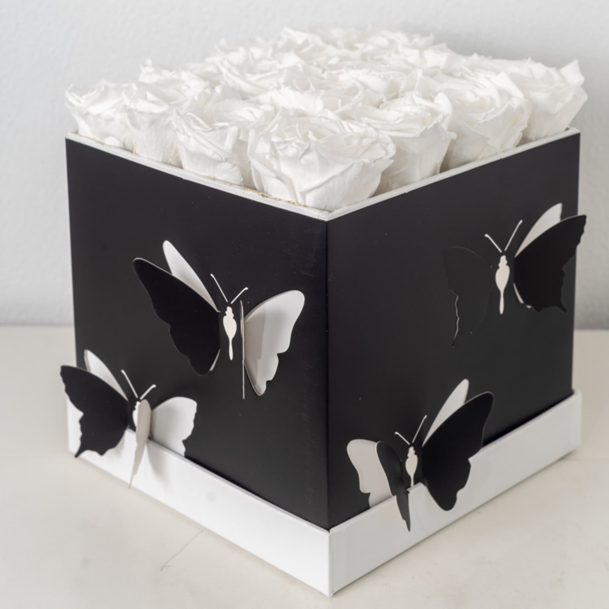Square black box with white roses on top and black-and-white butterfly decorations on the sides
