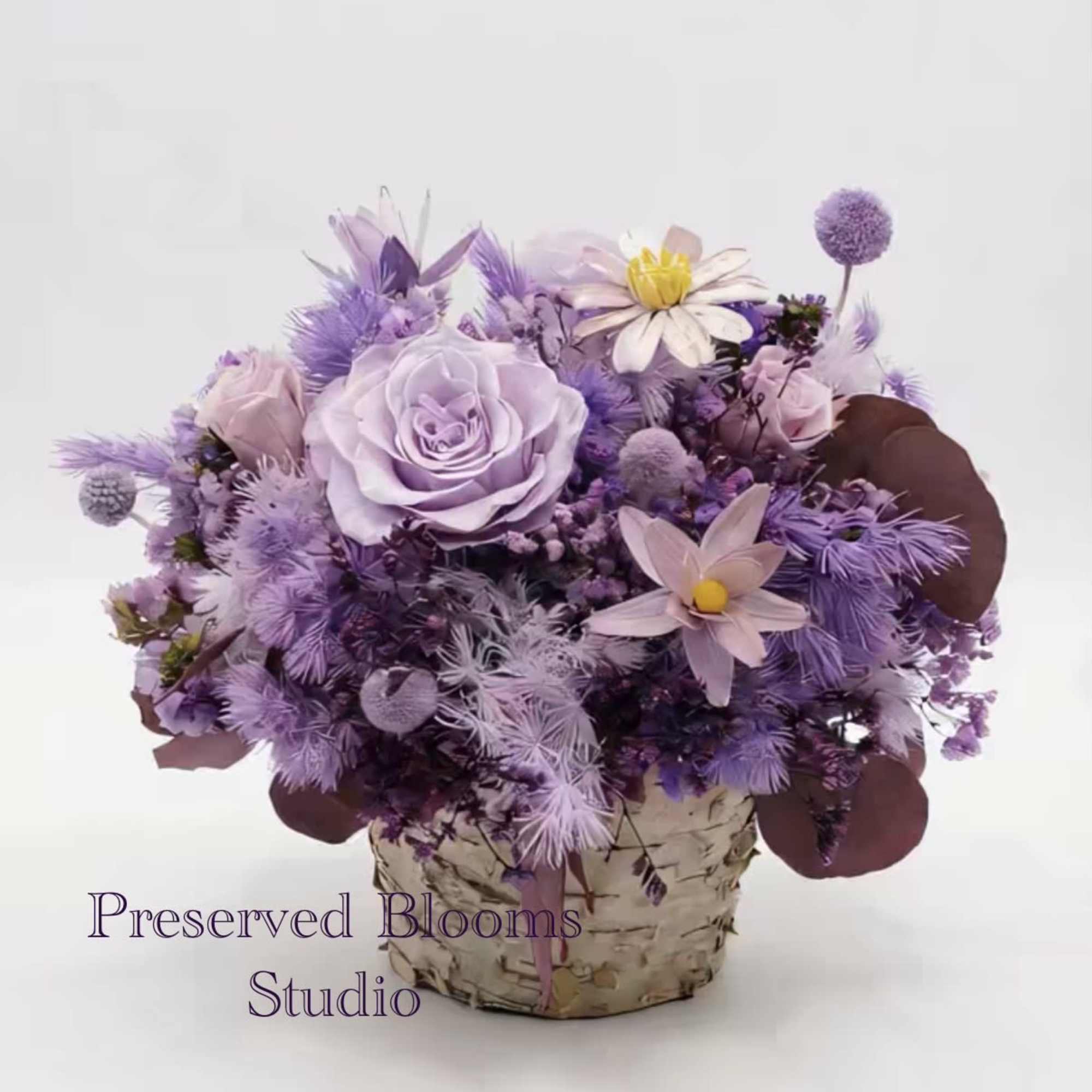 Lavender and purple flower arrangement with roses and daisies in a birch-wrapped pot