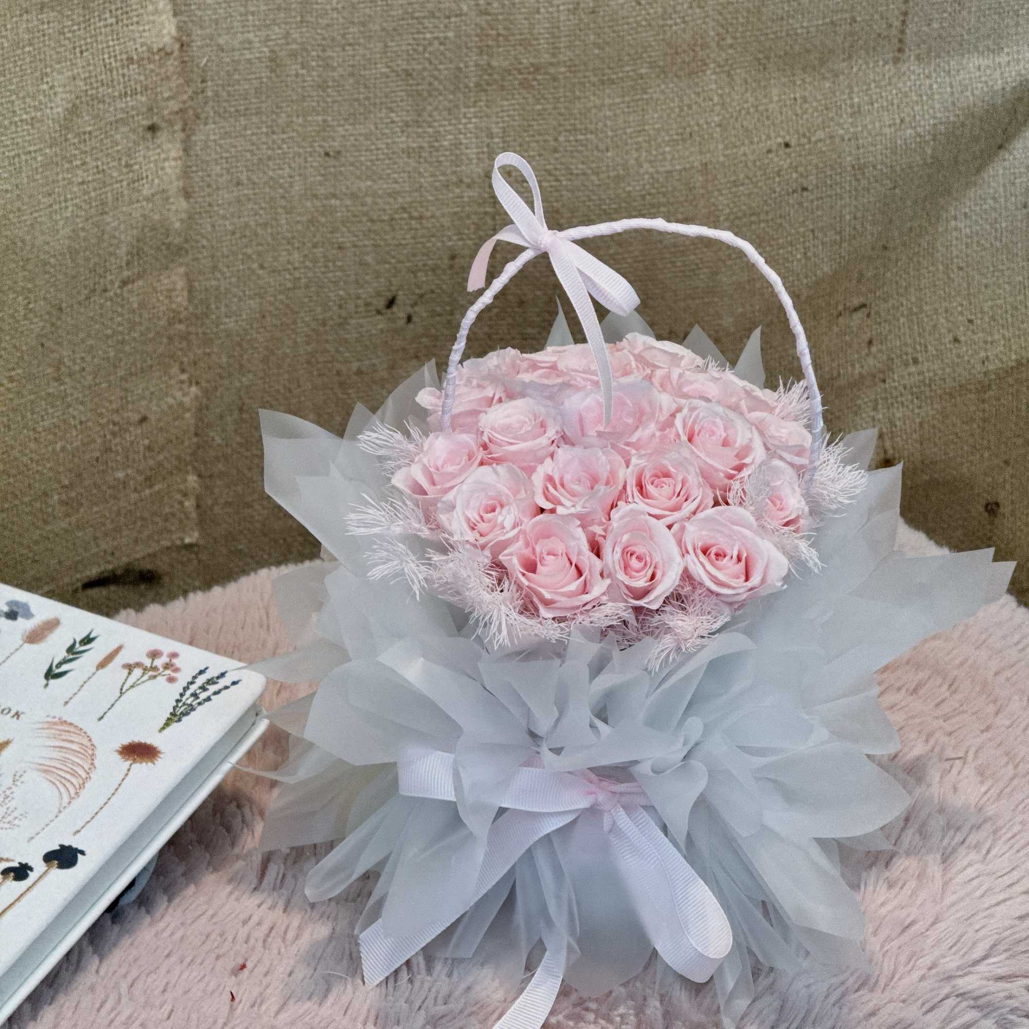Round arrangement of pale pink roses in a white ruffled wrap with a handle and bow