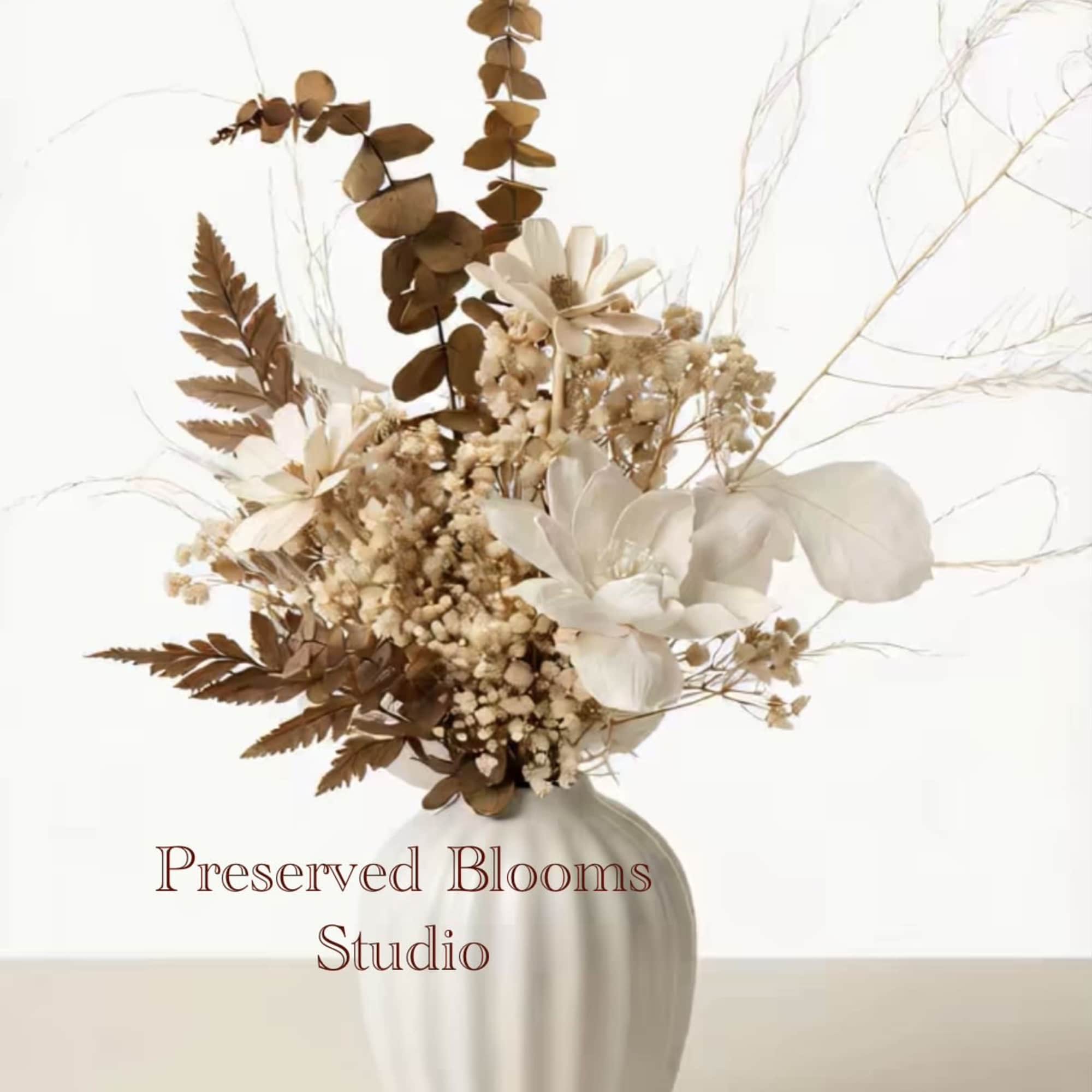 Neutral dried flower arrangement with white blooms and brown foliage in a white ceramic vase