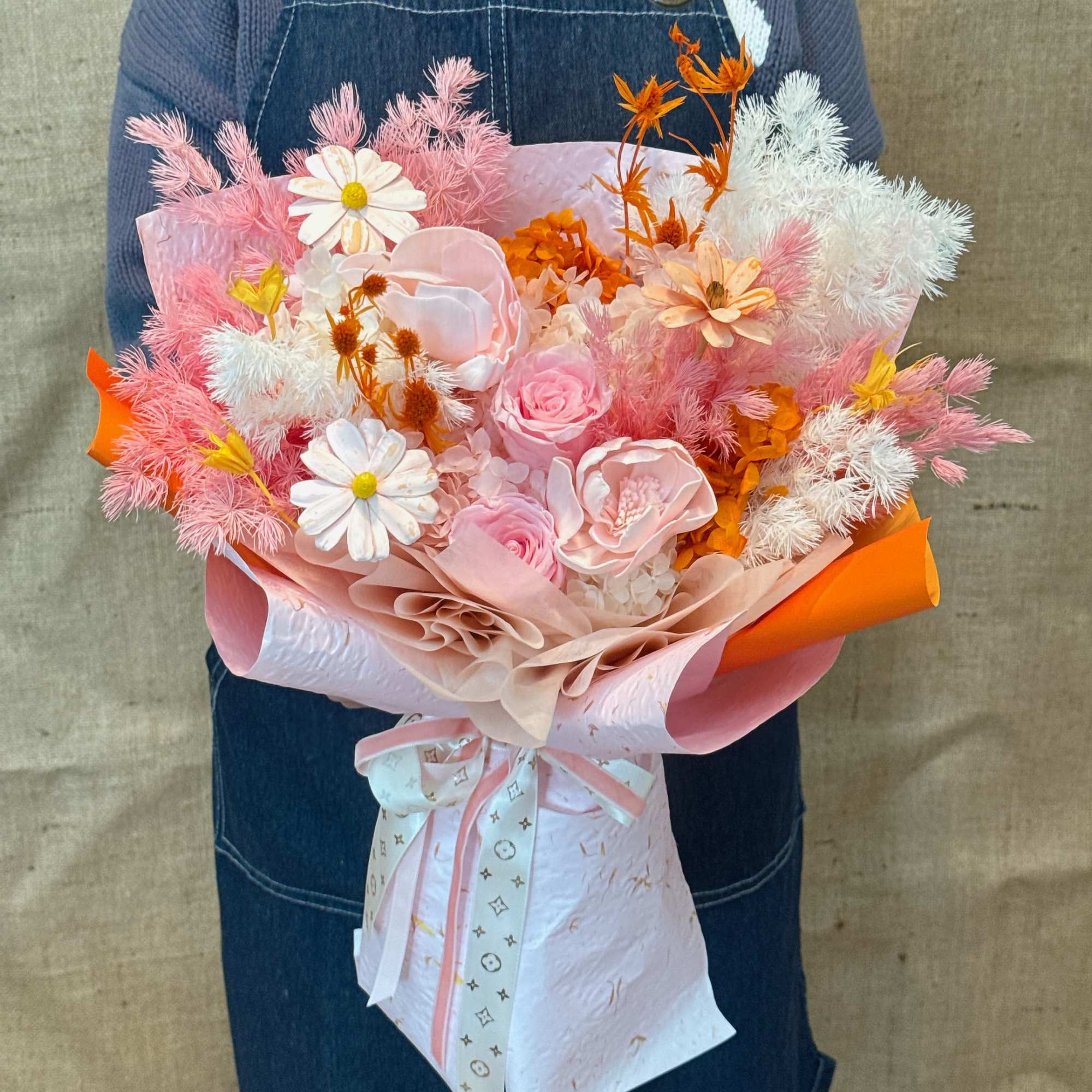 Large hand-tied bouquet of pink roses, white daisies, and orange accents wrapped in pink and orange paper