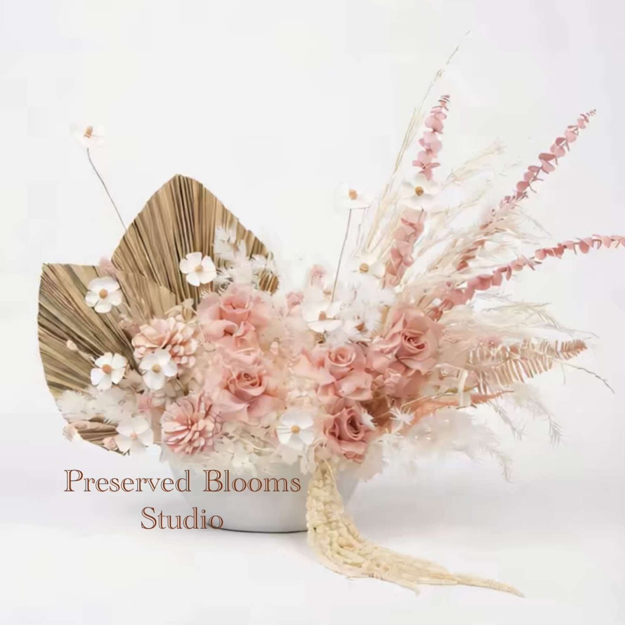 Low arrangement of blush roses, white daisy-like flowers, and dried accents in a white bowl.