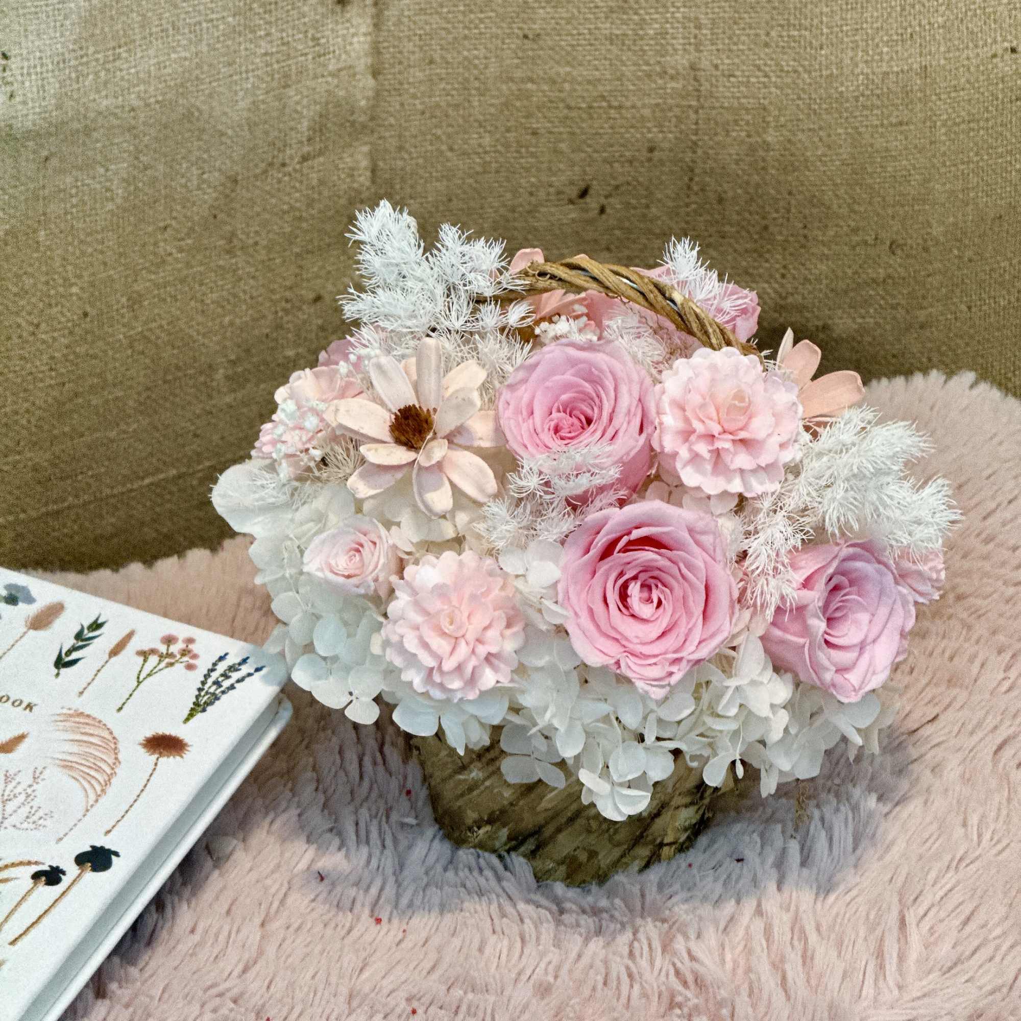 Small pink and white floral basket arrangement with roses and mums on a fuzzy surface