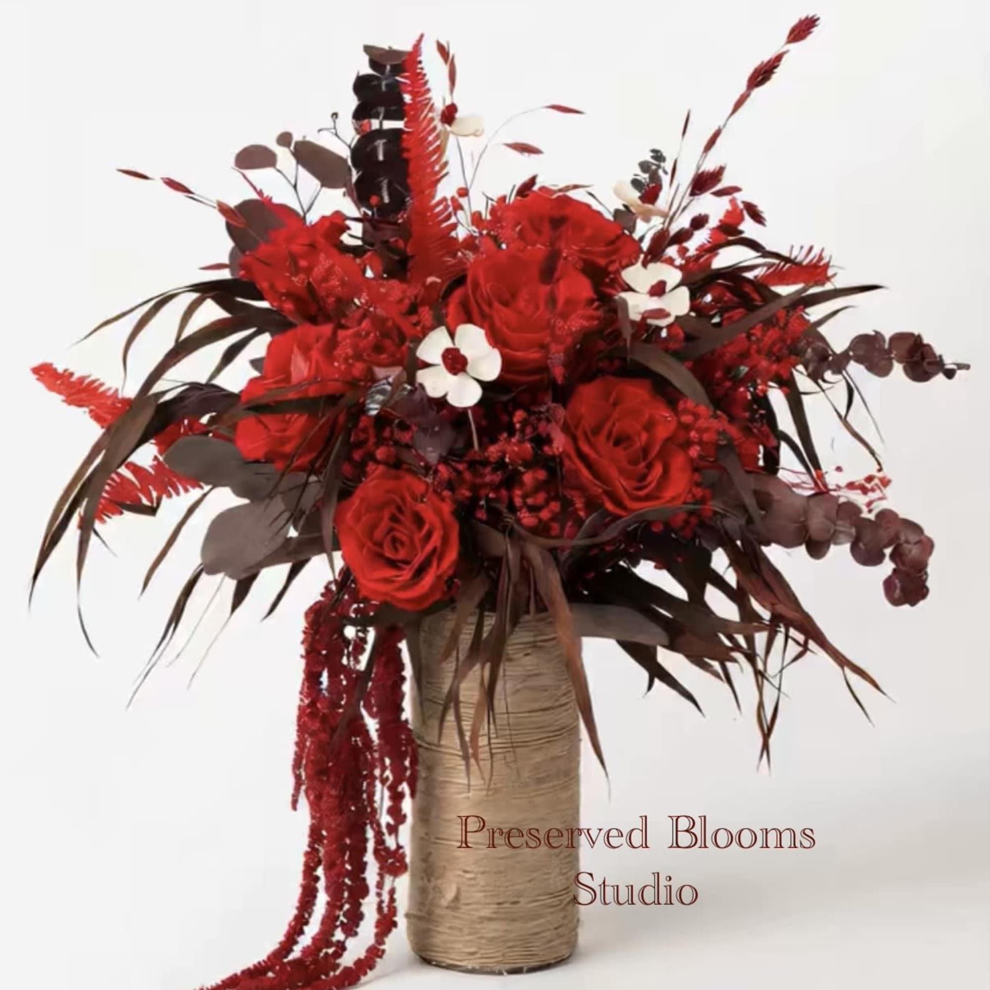 Tall arrangement of deep red roses and berries in a twine-wrapped cylinder vase