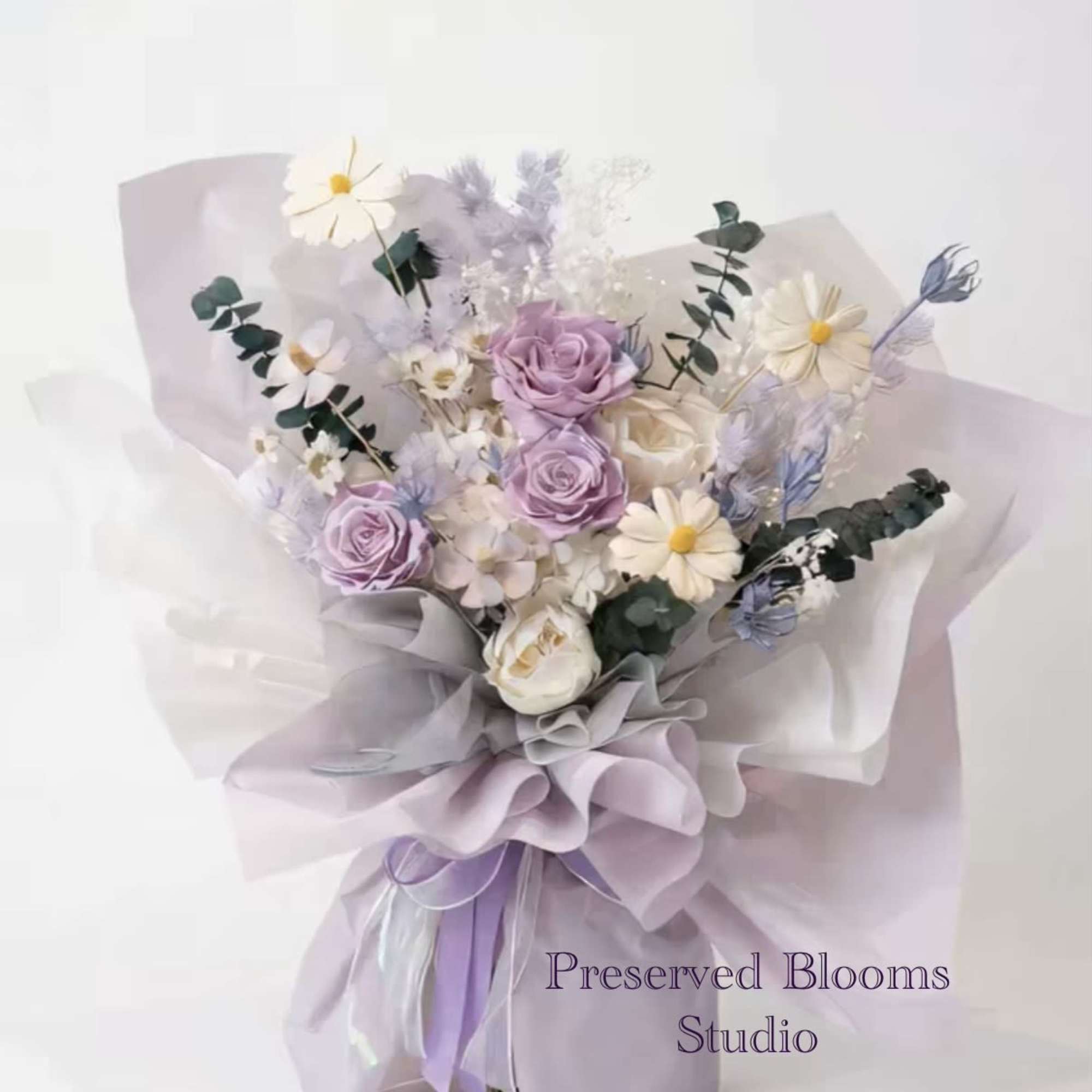 Hand-tied bouquet of lavender roses and white daisies wrapped in layered lilac and white paper.