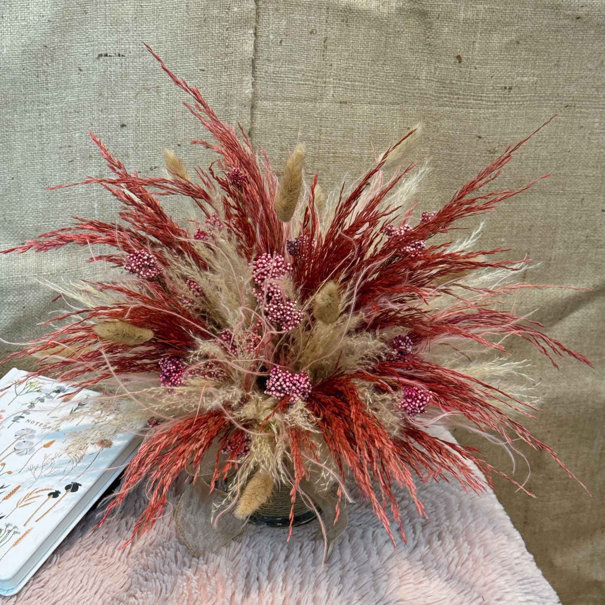 Dried red and beige grasses with pink berry stems arranged in a clear glass vase