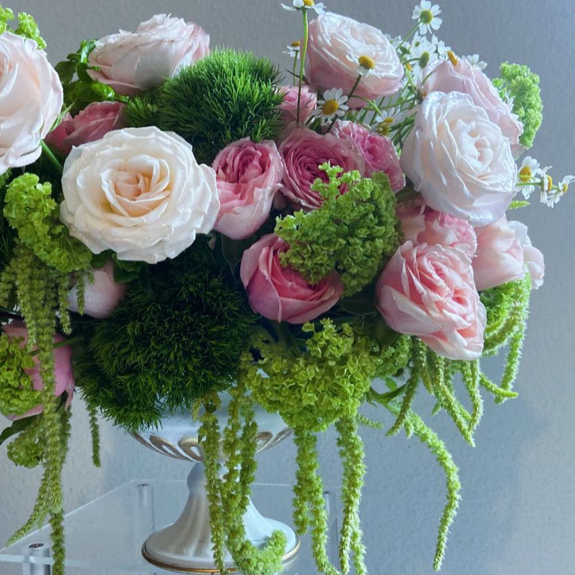 Low arrangement of pale pink and white roses with green accents in a white pedestal bowl