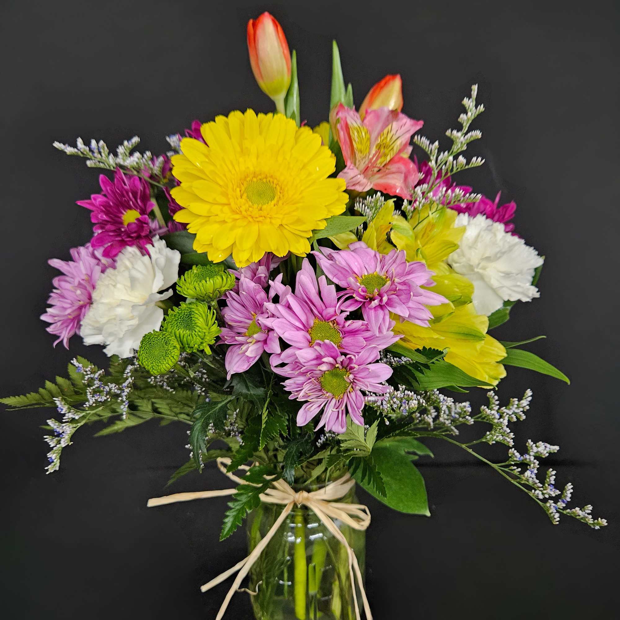Mixed spring bouquet with yellow gerbera, tulips, carnations and daisies in a glass jar vase.