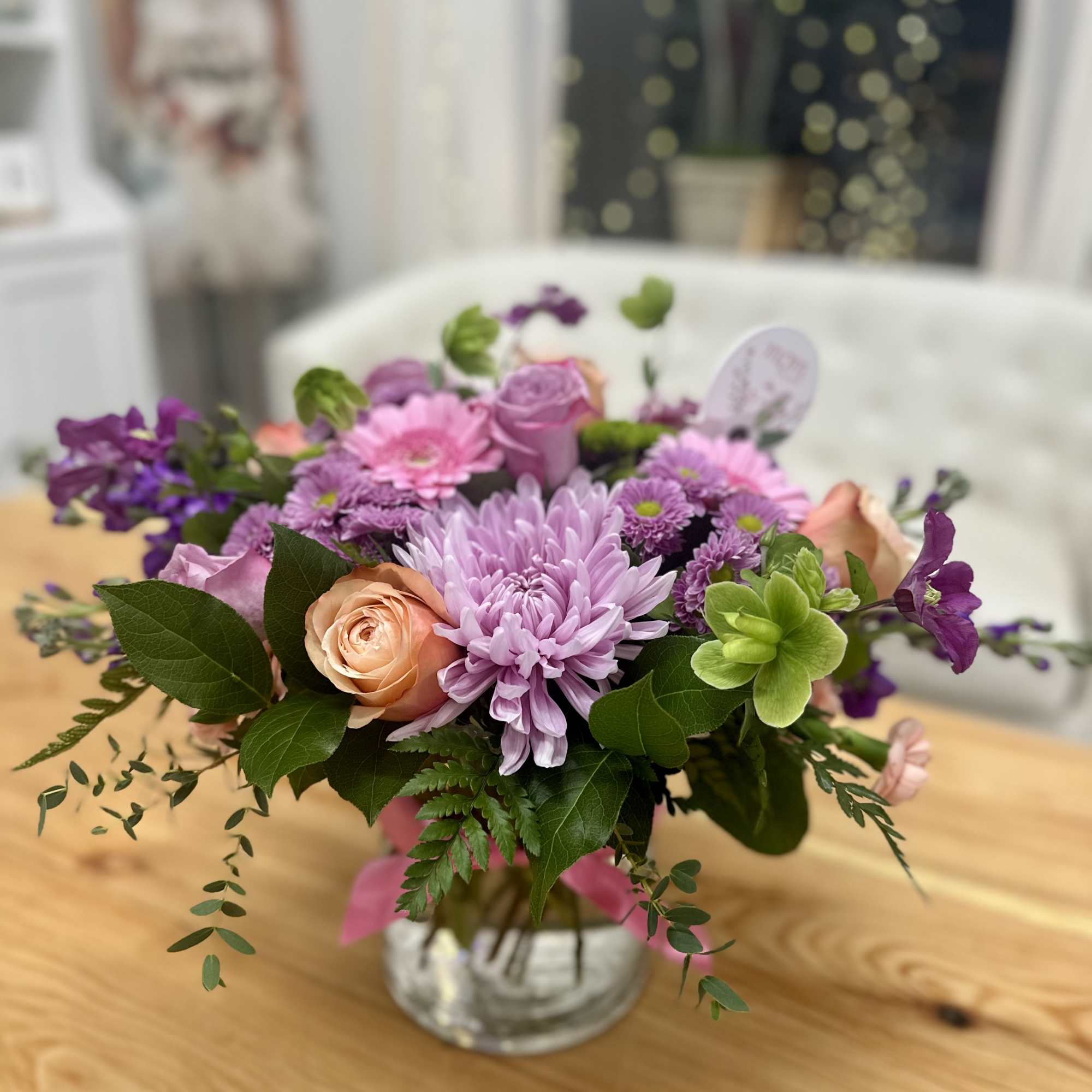 Low glass vase of pink and purple flowers with roses, gerbera daisies, and a green succulent.
