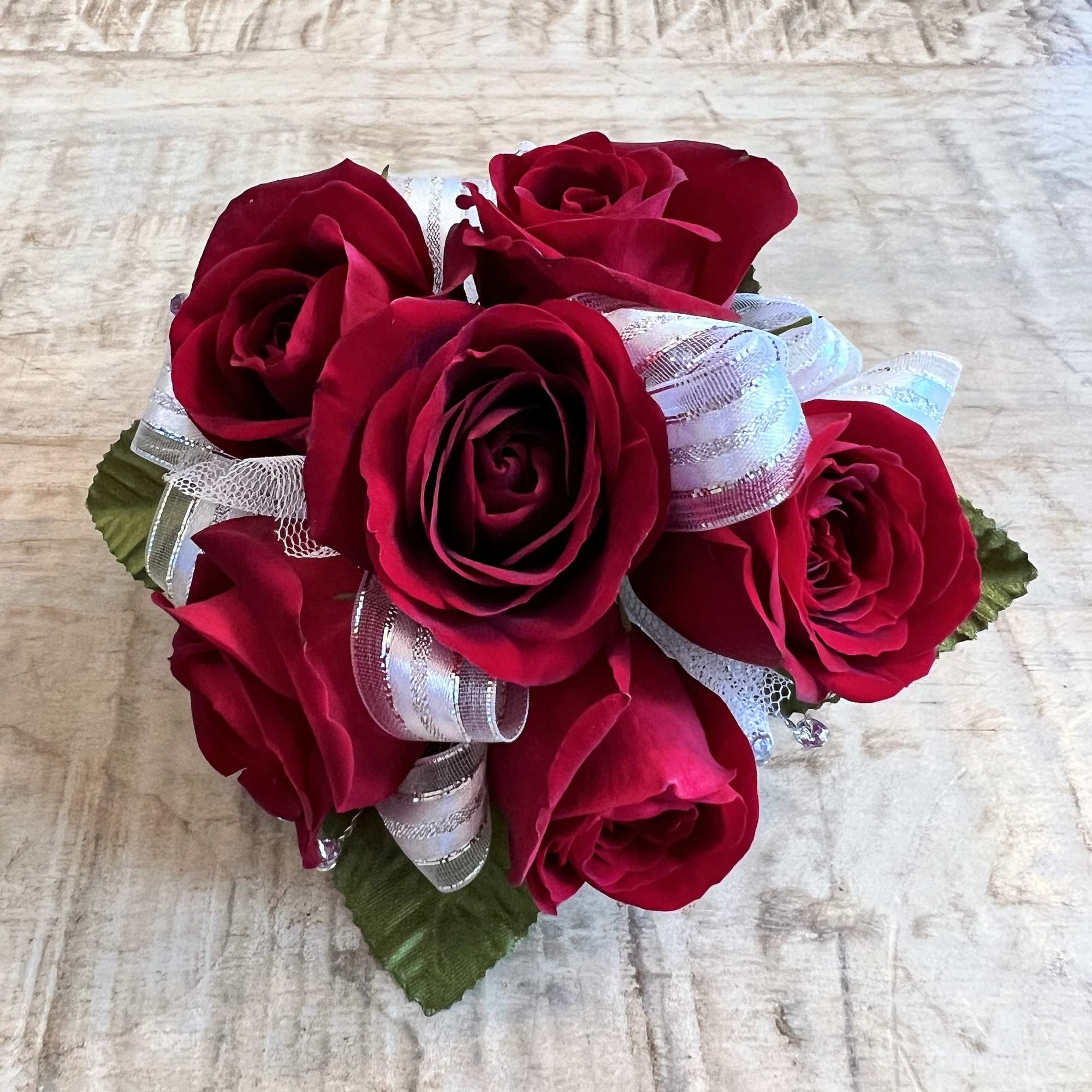 Compact cluster of red roses with silver and white ribbon in a round posy on a light wood surface