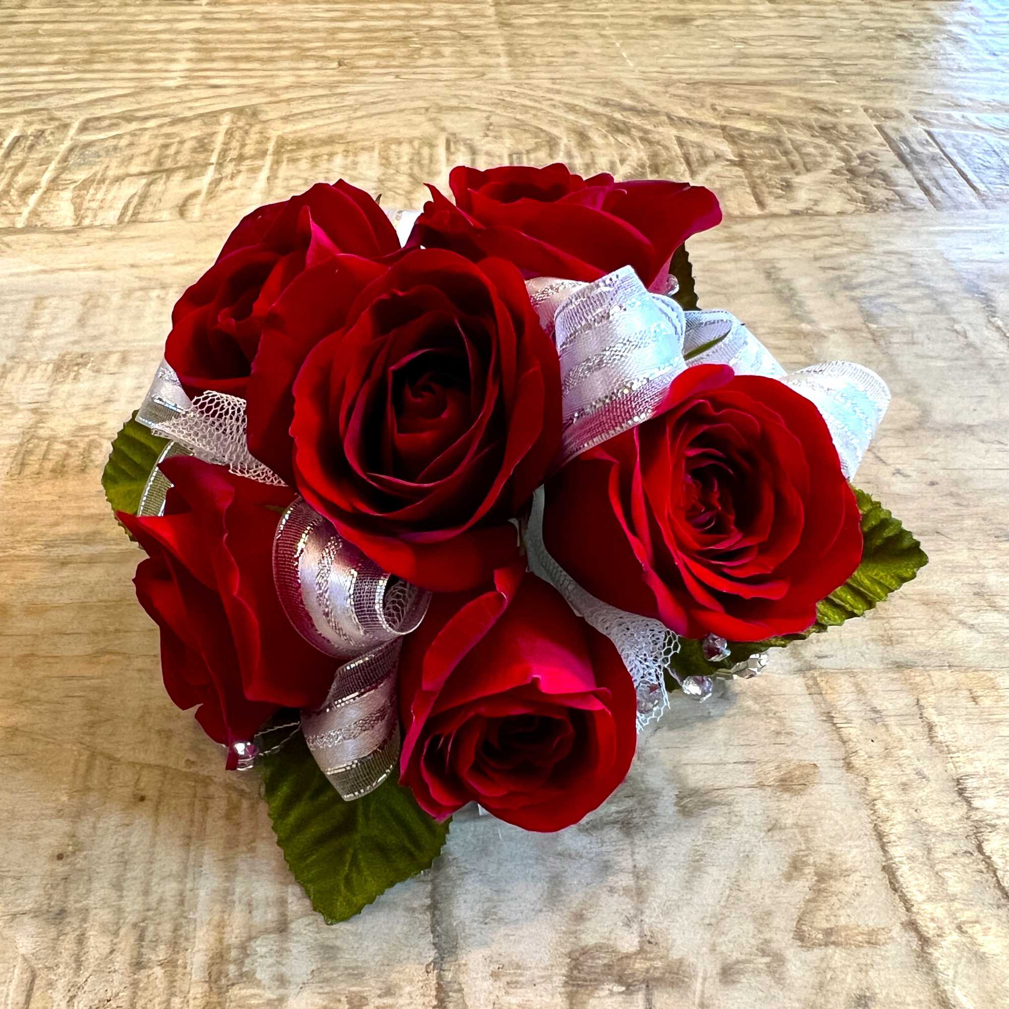 Small cluster of red roses accented with white sheer ribbon on a wood surface