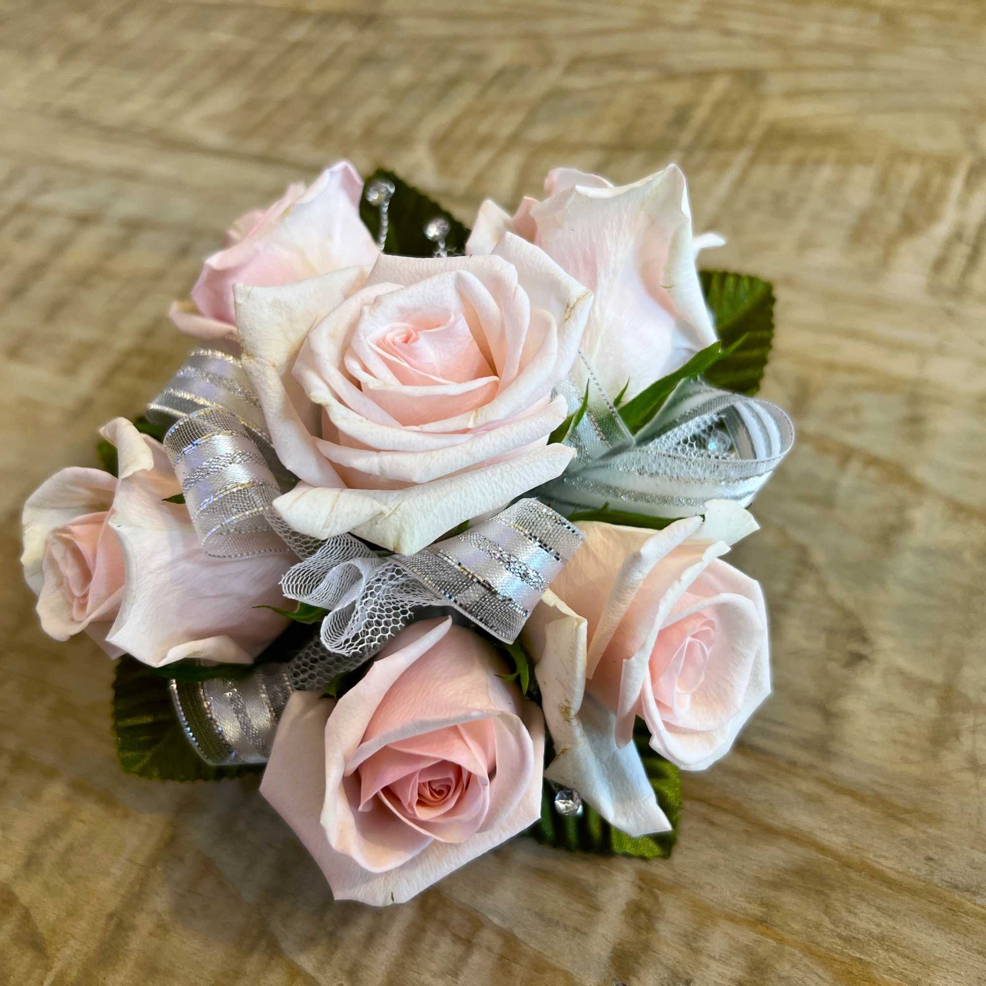 Cluster of pale pink roses with silver ribbon accents arranged as a small corsage.