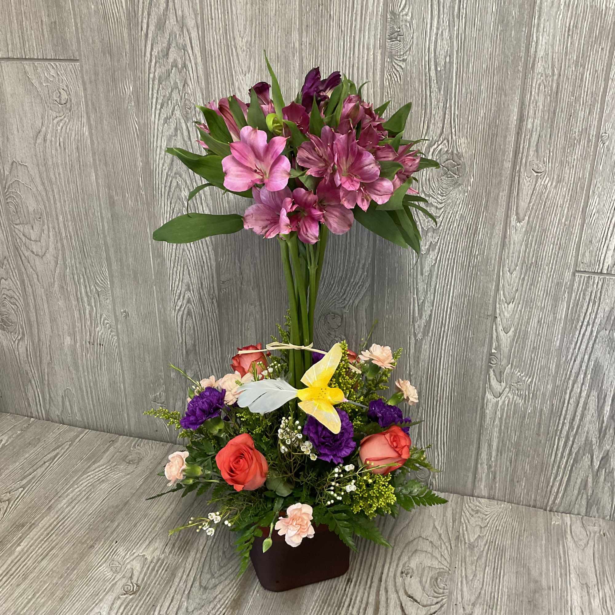 Two-tier arrangement with pink alstroemeria, roses, purple blooms and a yellow lily in a red vase
