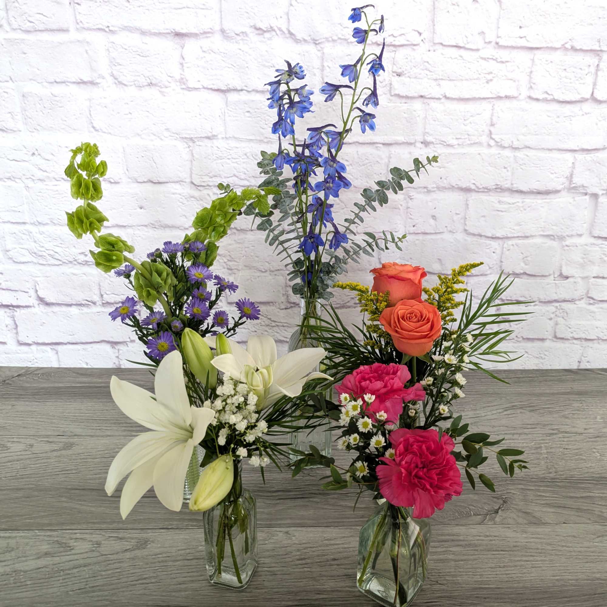 Three mixed flower arrangements in clear glass vases on a table