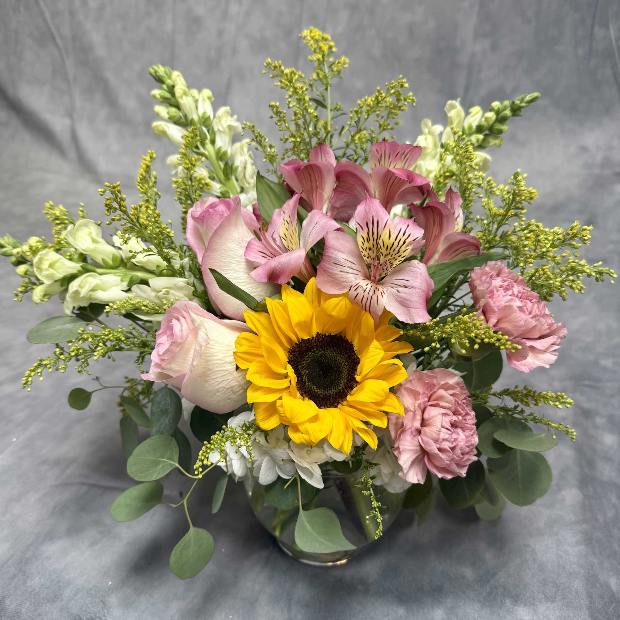 Bouquet of sunflowers, pink alstroemeria, and roses in a glass vase