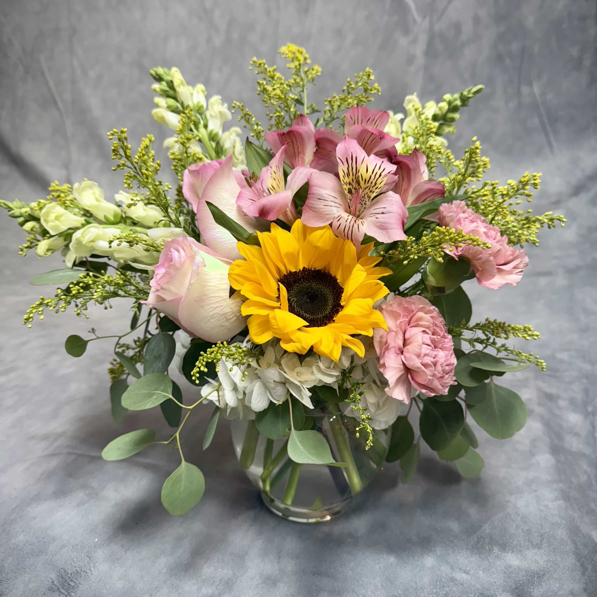 Bouquet of sunflowers, pink alstroemeria, and carnations in a glass vase